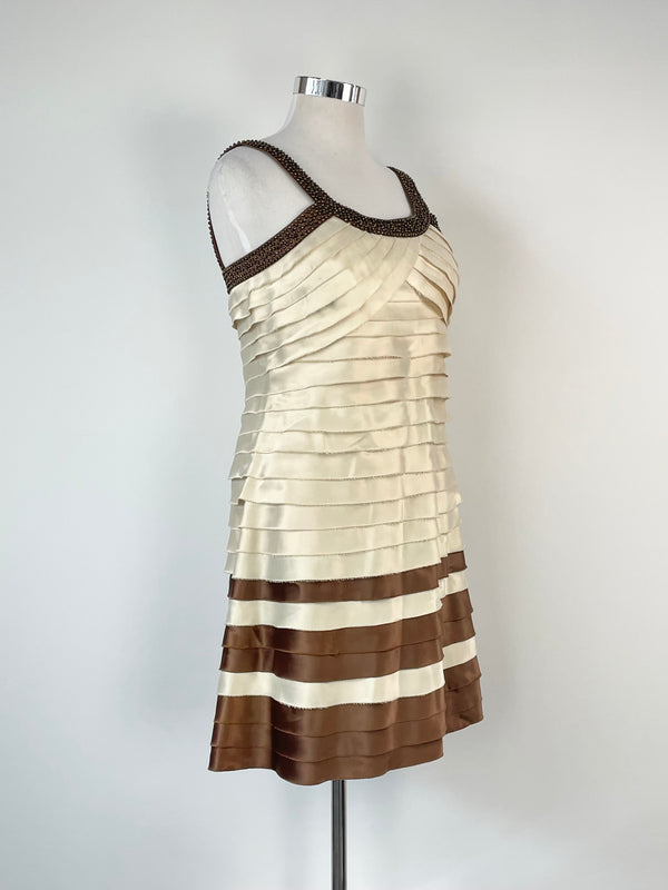 A mannequin displaying a beige and brown striped cocktail dress with a v-neck and sleeveless top, featuring a layered design.