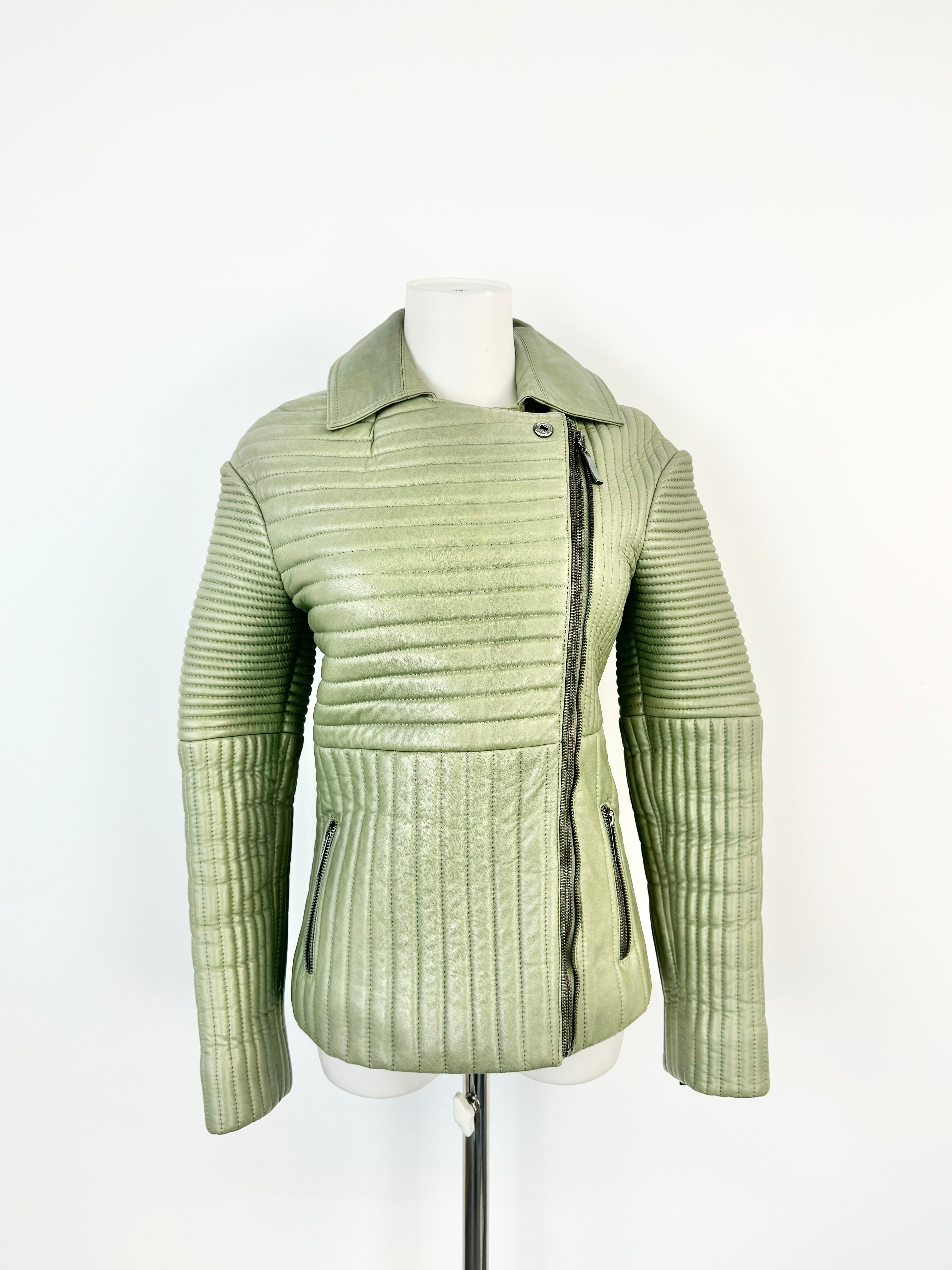 A sage green quilted leather jacket with an symmetrical zipper and pockets at the waist, displayed on a mannequin against a white background.