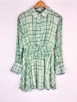 Green checkered dress on a hanger against a white background