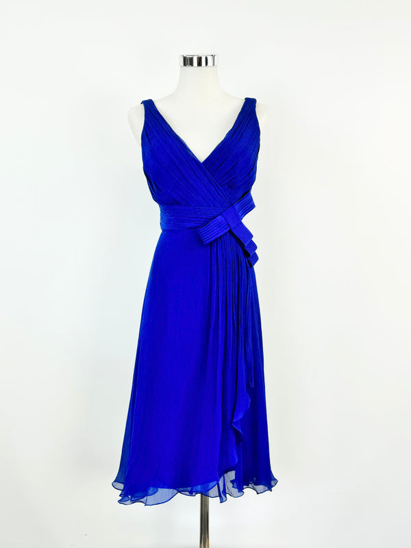 A blue chiffon silk midi dress with a v-neck and back, featuring a stitched bow embellishment beneath the bust and a gently blossoming skirt, displayed on a mannequin.
