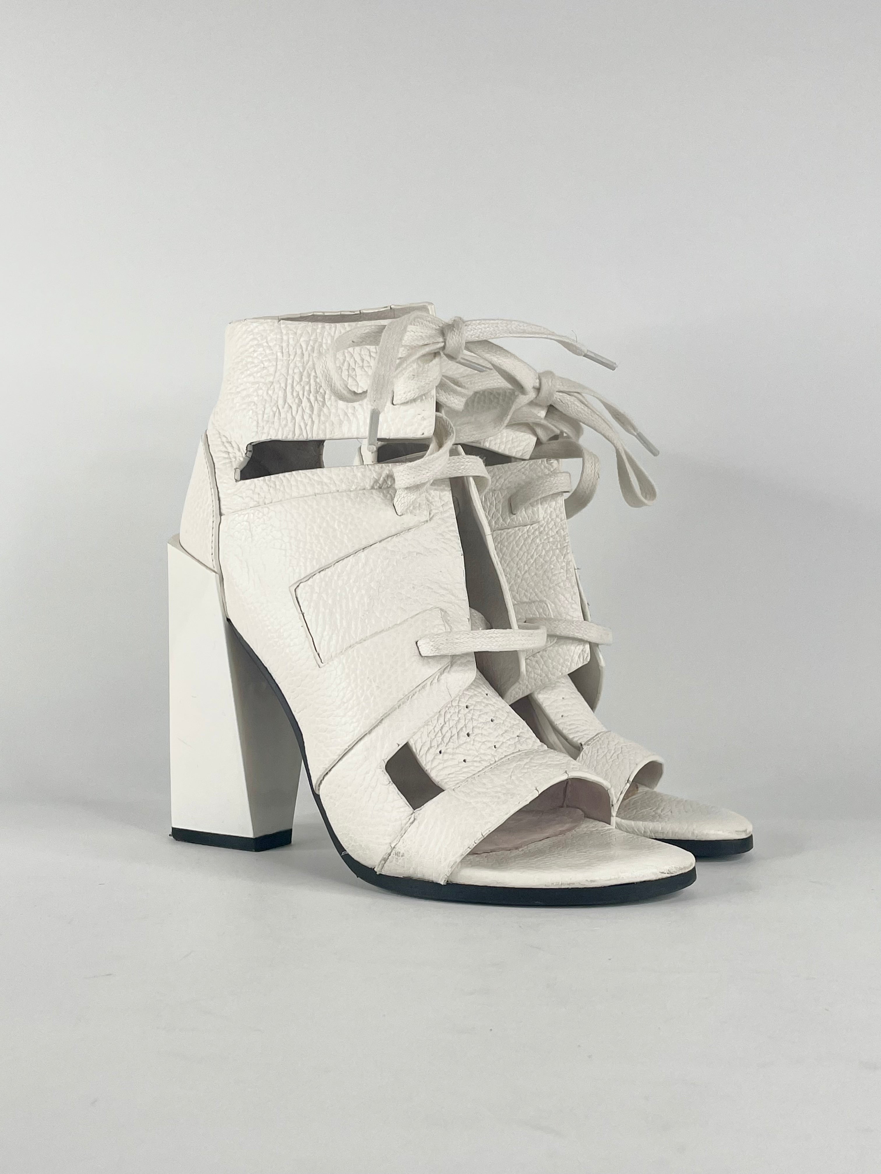 A pair of white grained leather lace-up heels with a peep toe, displayed against a plain background.