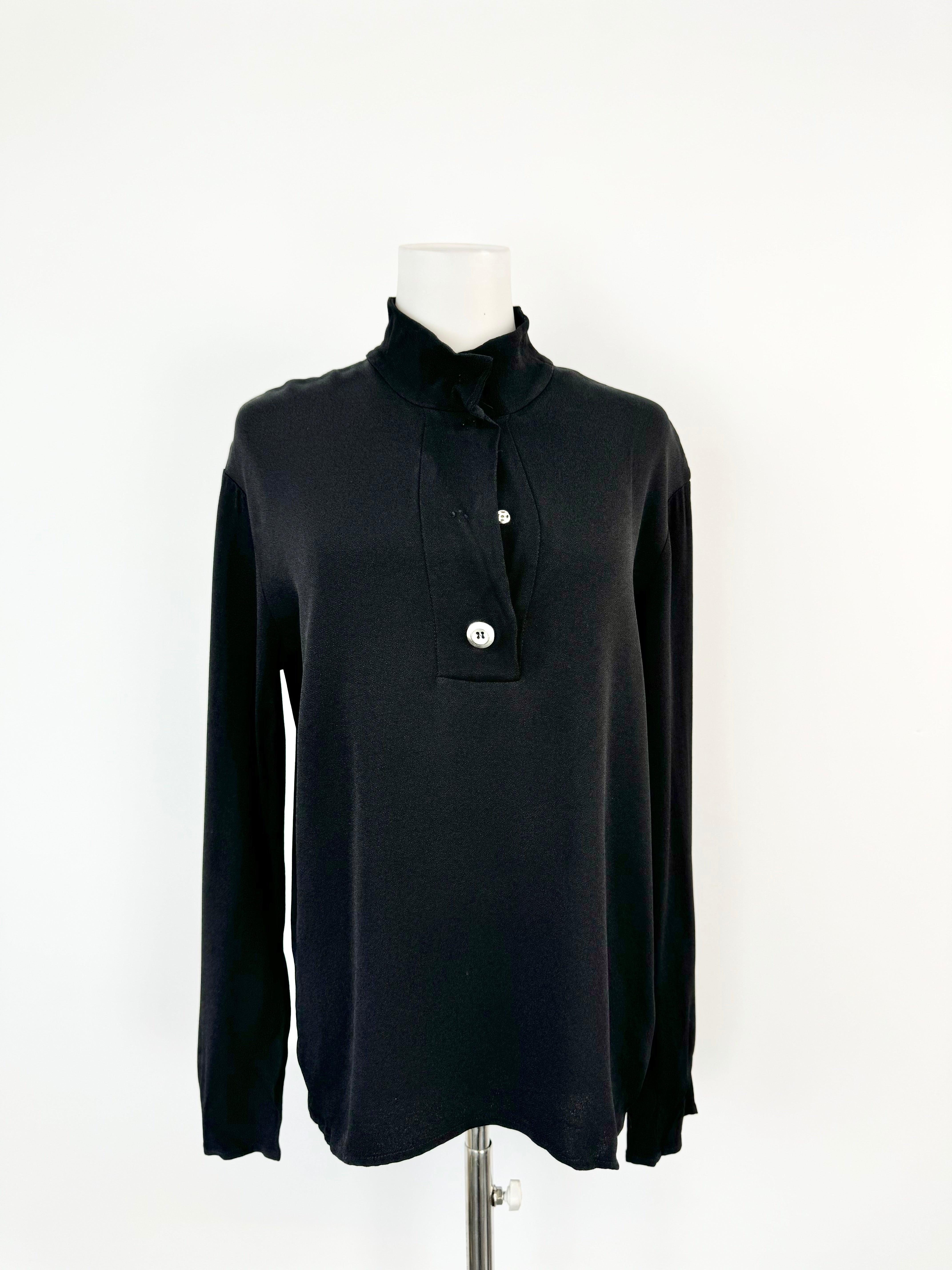 A black long sleeve top with a high neckline and snap buttons on a mannequin. The buttons are partially sewn on one side.