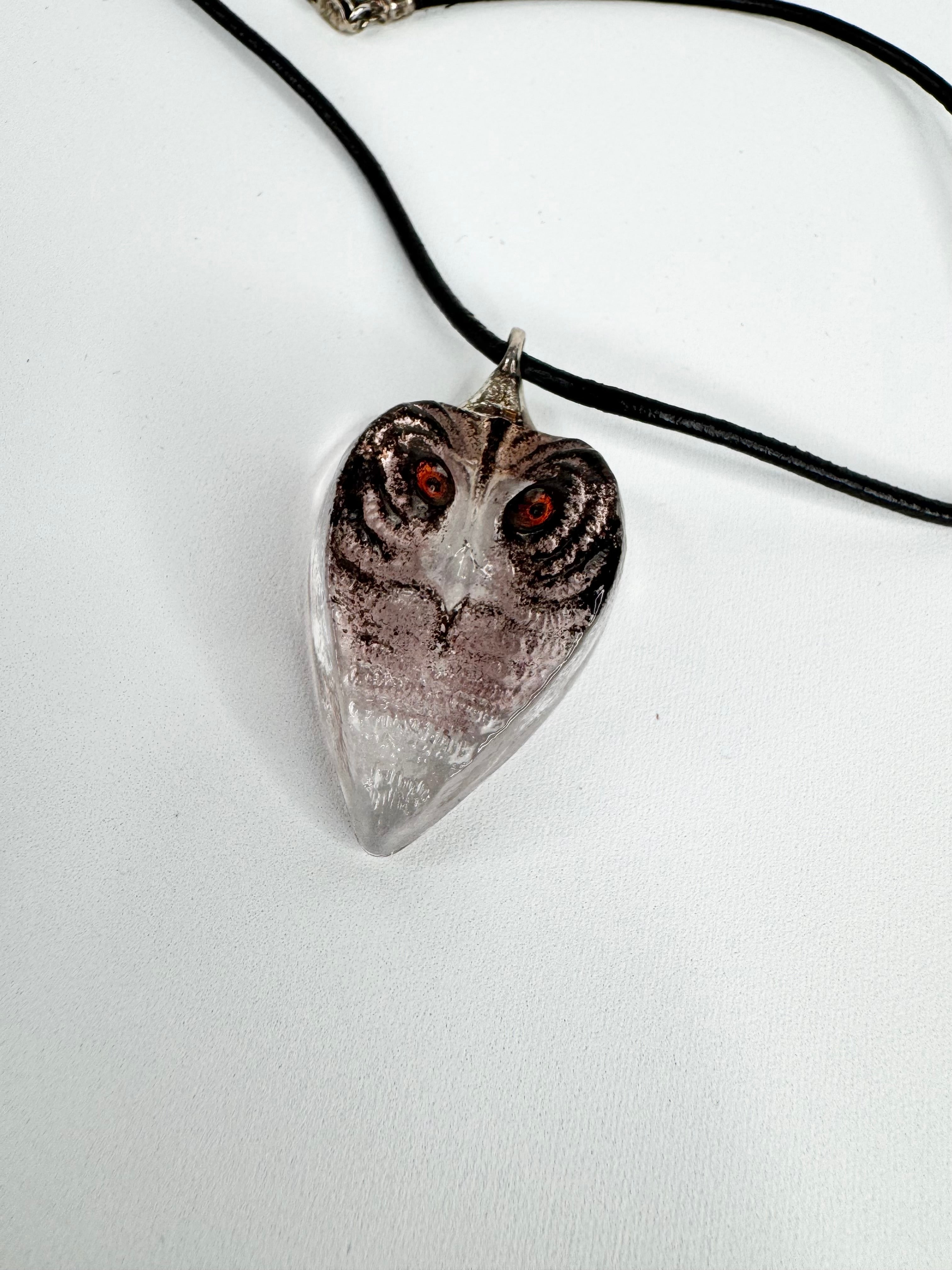 Heart-shaped owl pendant on a black cord against a white background