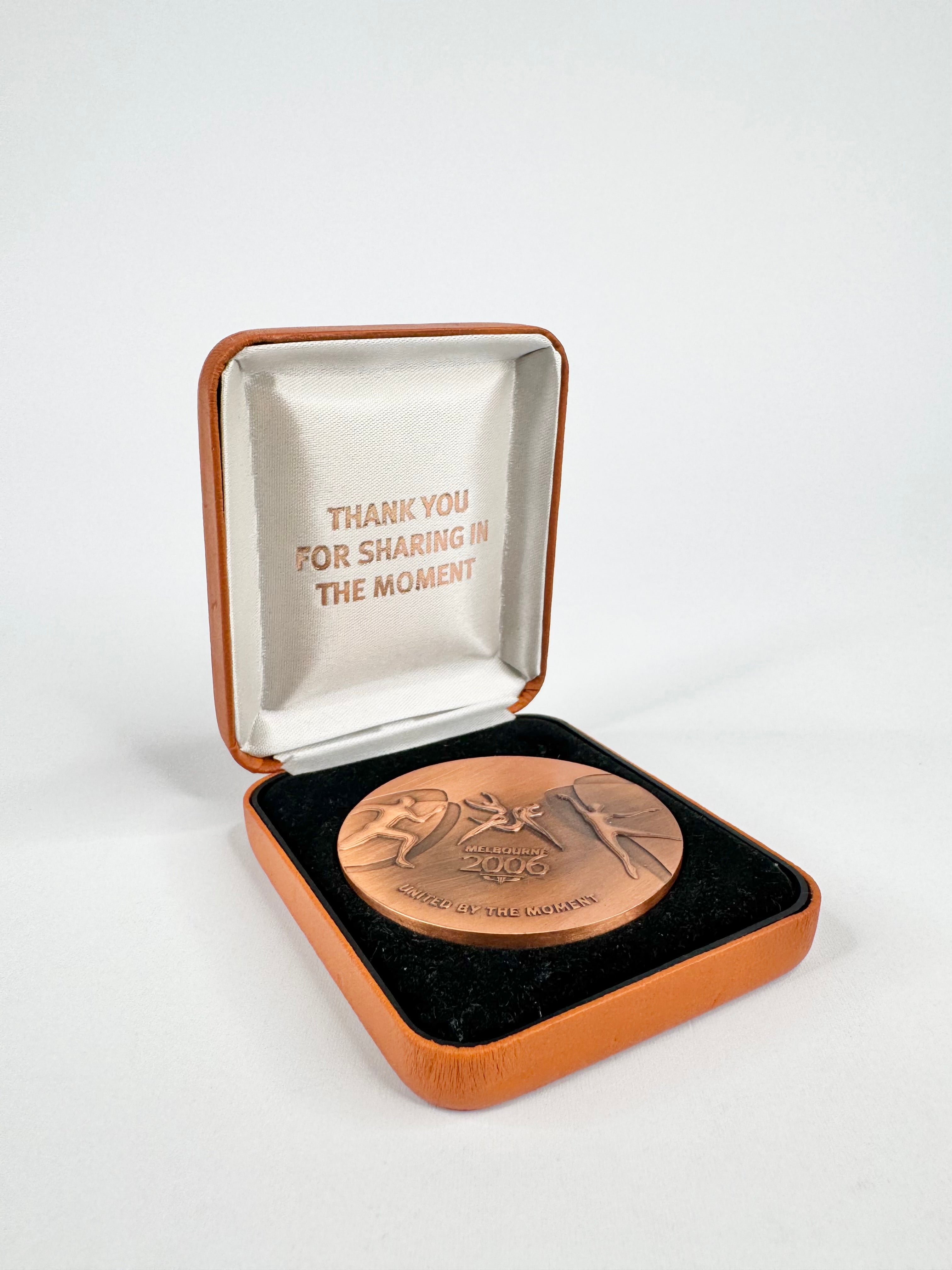 Bronze medal in a wooden box with a white interior, featuring engraved text.