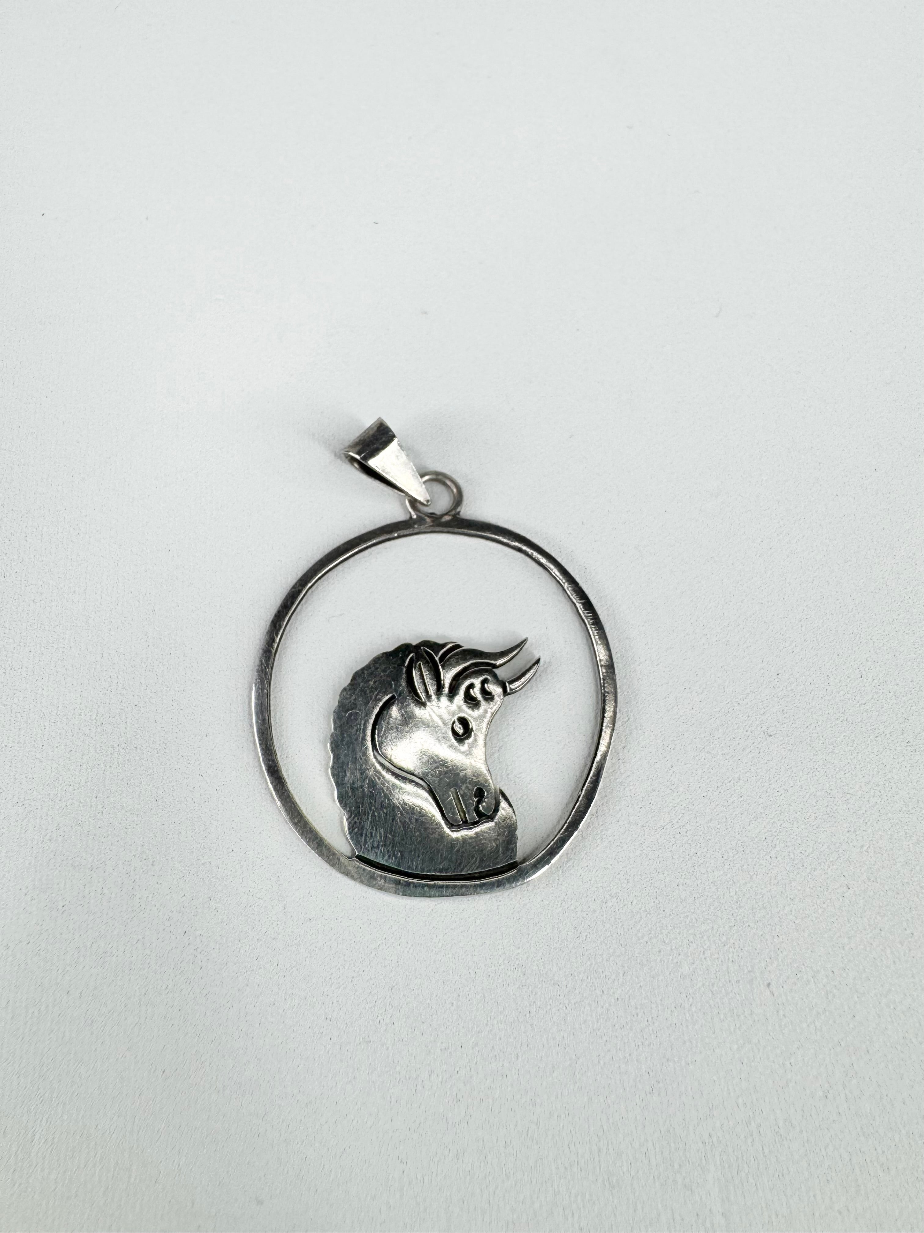 Silver pendant with unicorn design on a light gray background