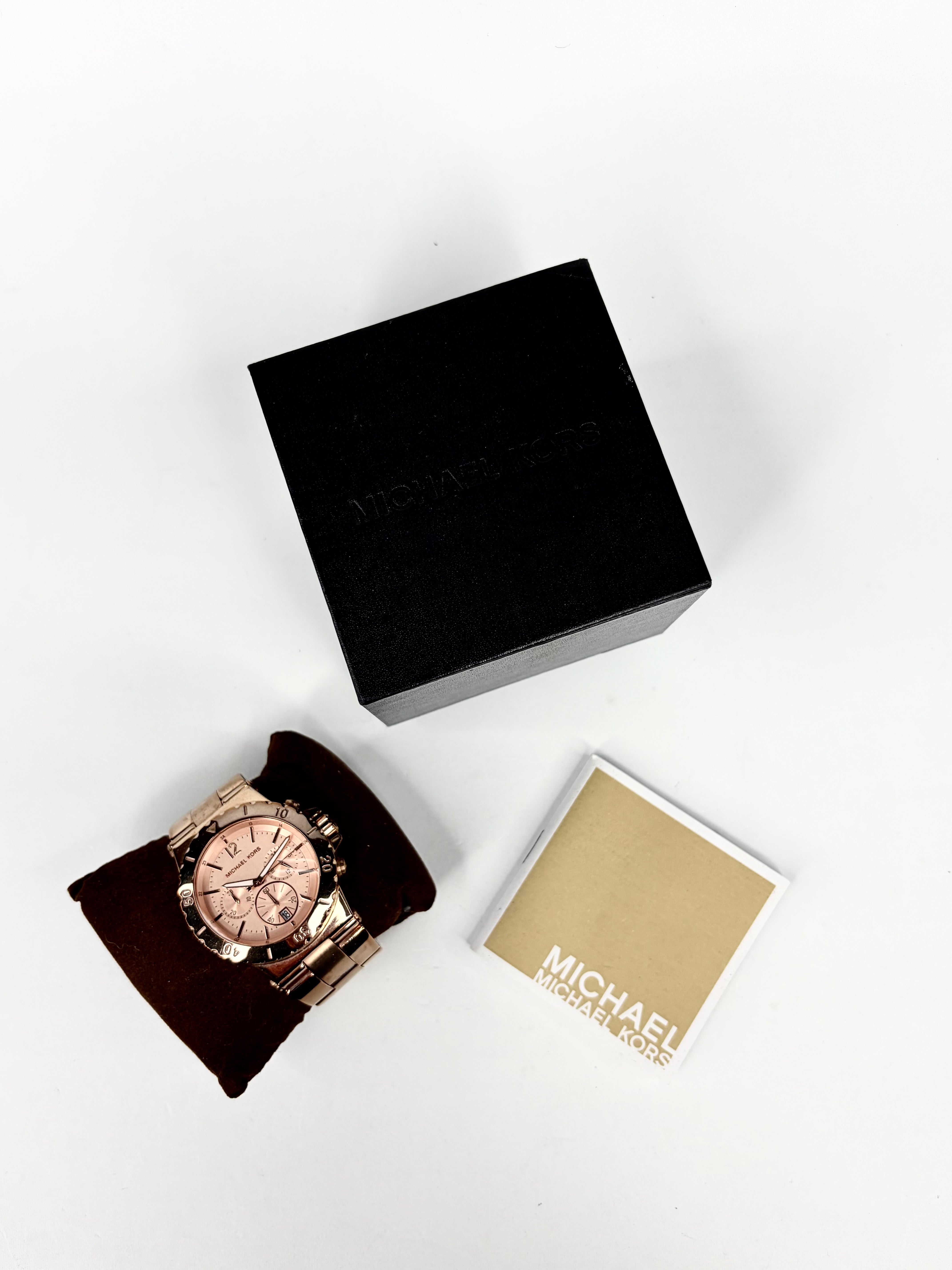Rose gold watch with black box and beige card on a white background