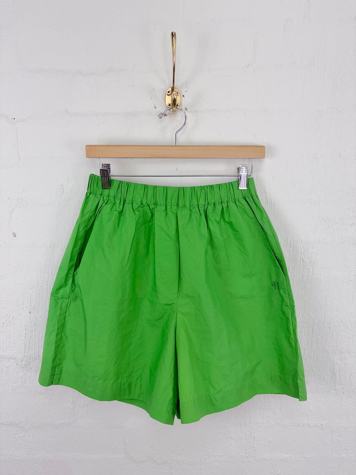 Bright green athletic shorts hanging from a wooden hanger on a white brick wall.