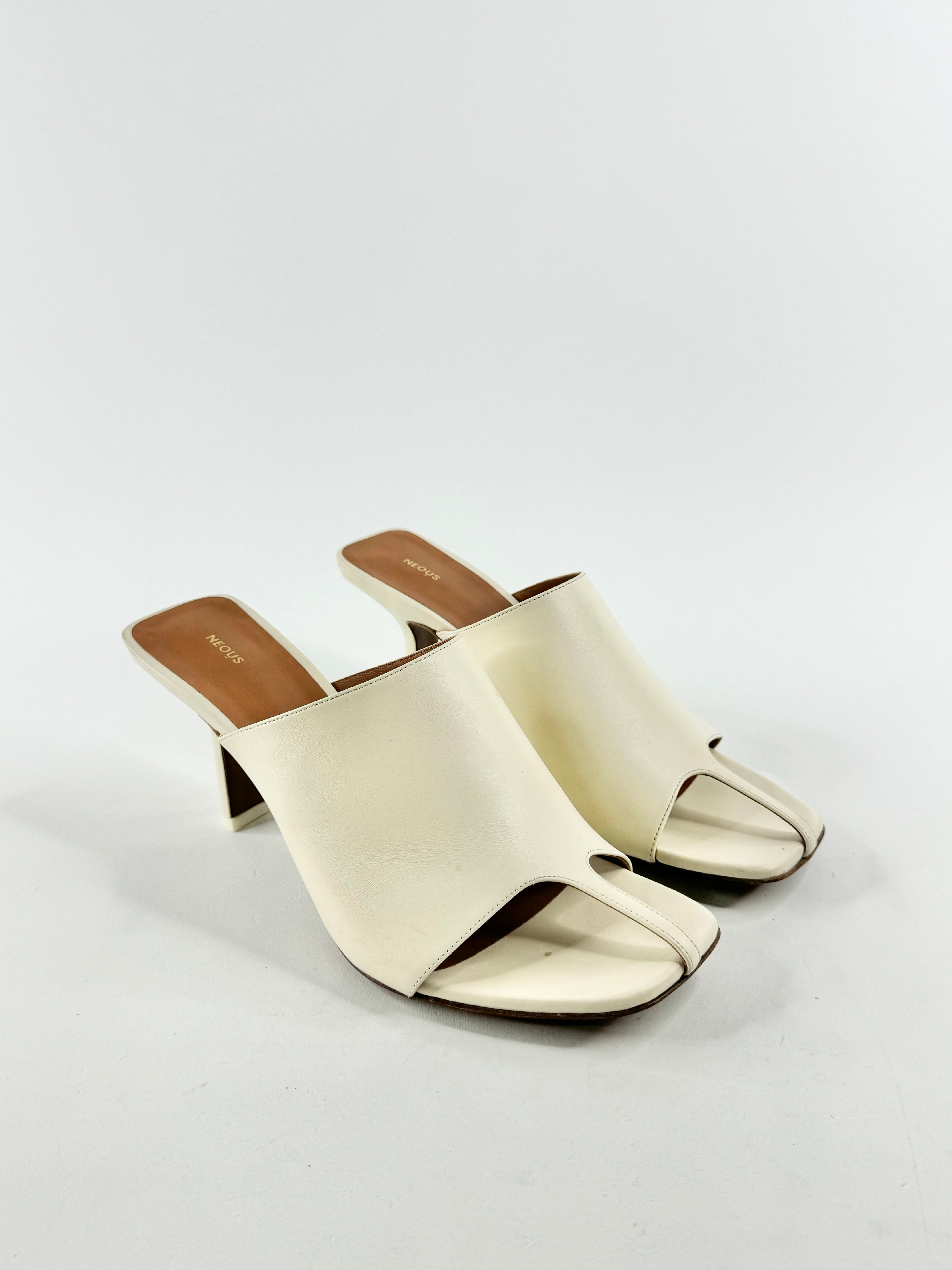 A pair of cream-colored Neous 'Jamuel' T-Bar mules with a t-bar feature at the toe and a low heel, displayed against a white background.
