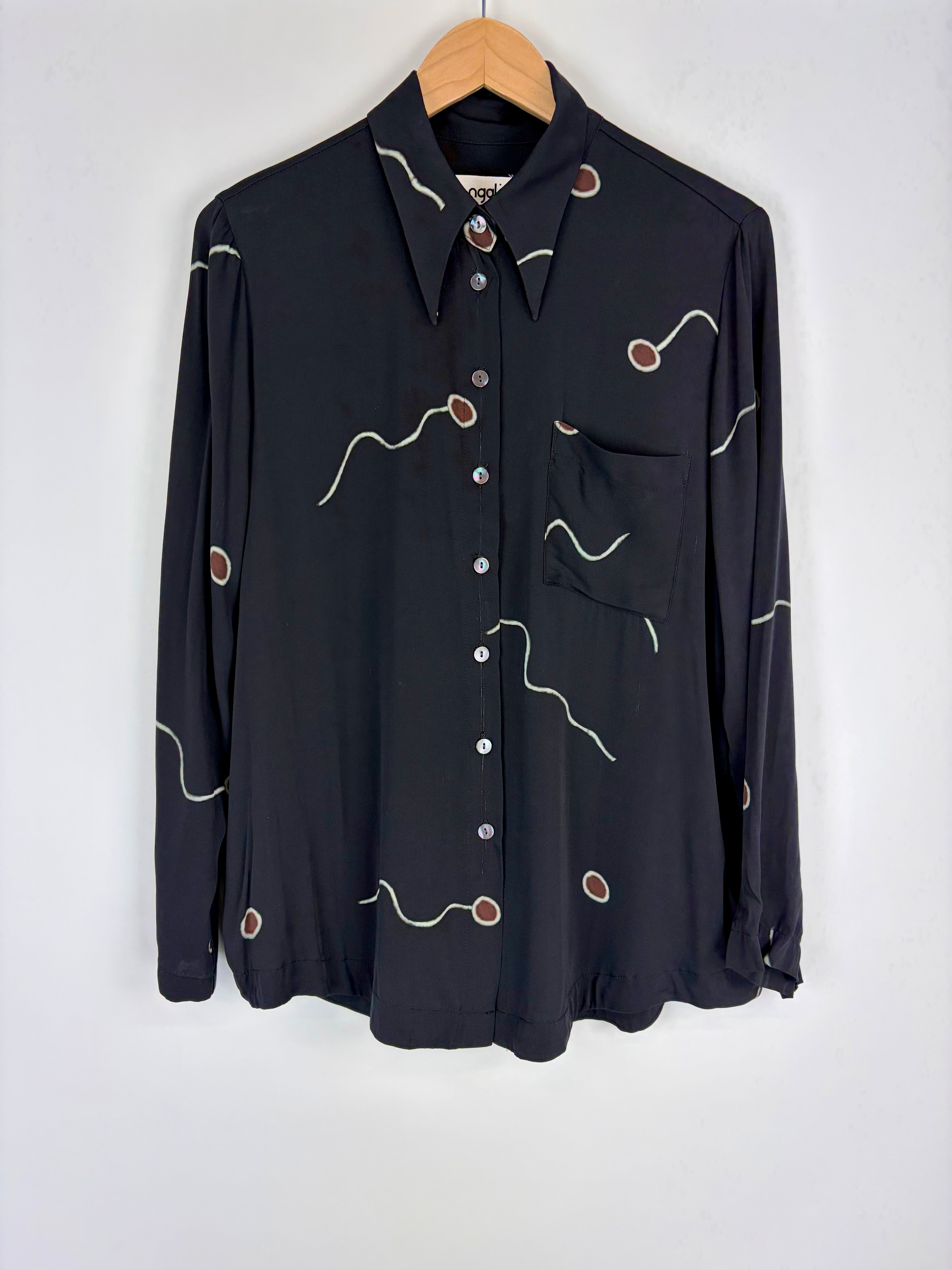 Black shirt with decorative buttons and stitching on a hanger against a white background