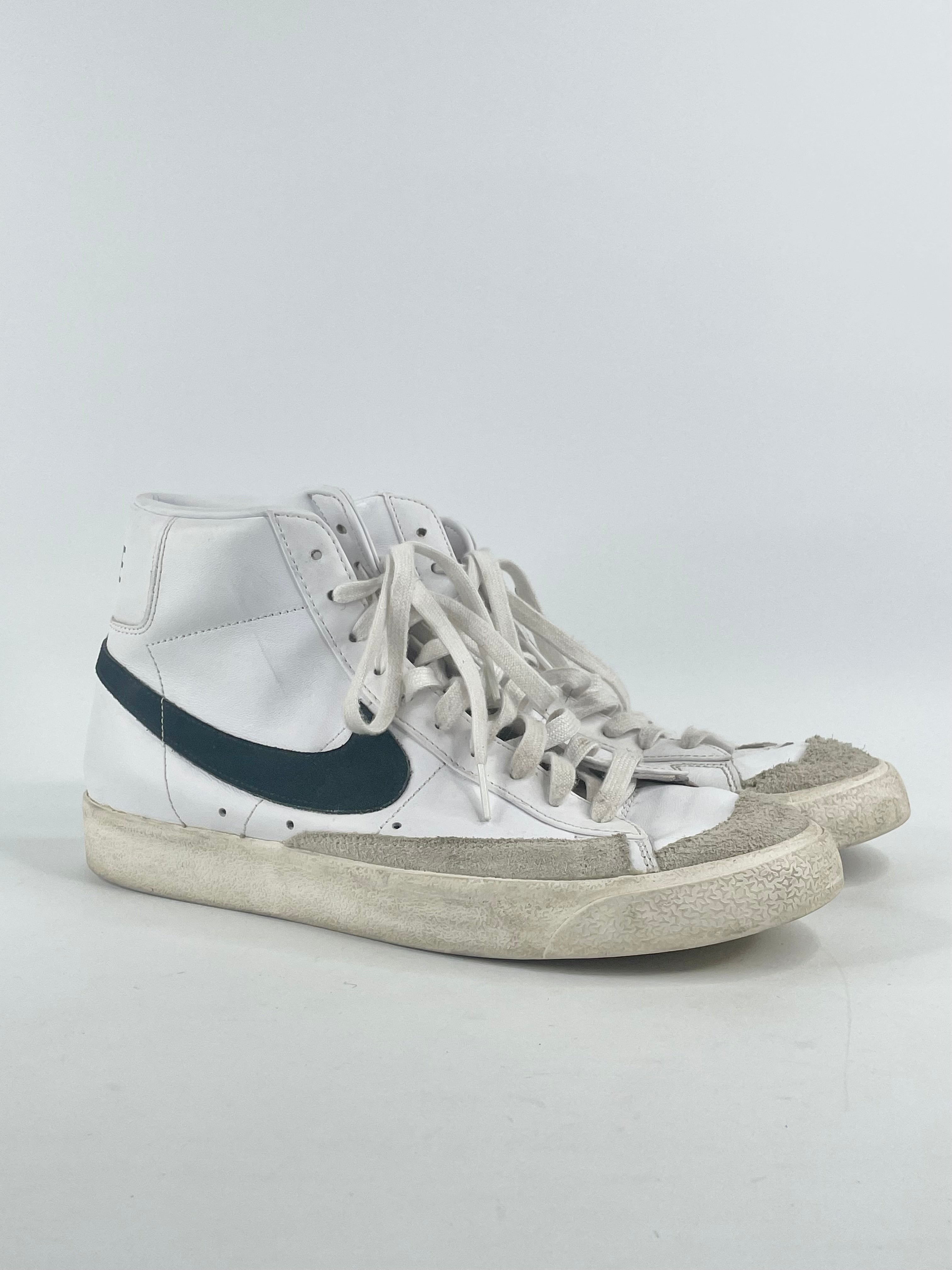 A pair of white Nike Blazer Mid '77 vintage-style high-top sneakers with visible wear on the soles.