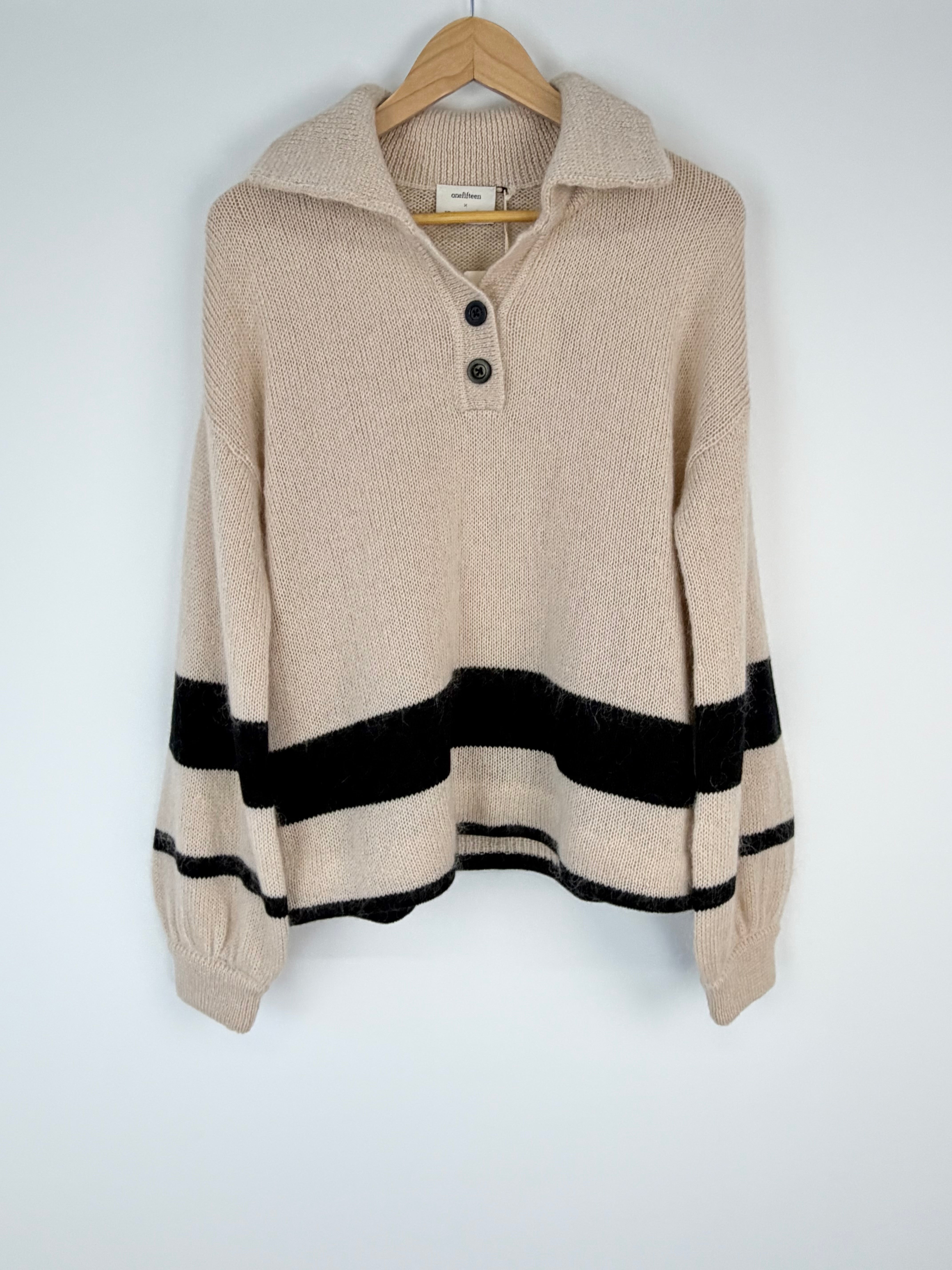 Beige sweater with black stripes on a wooden hanger against a white background
