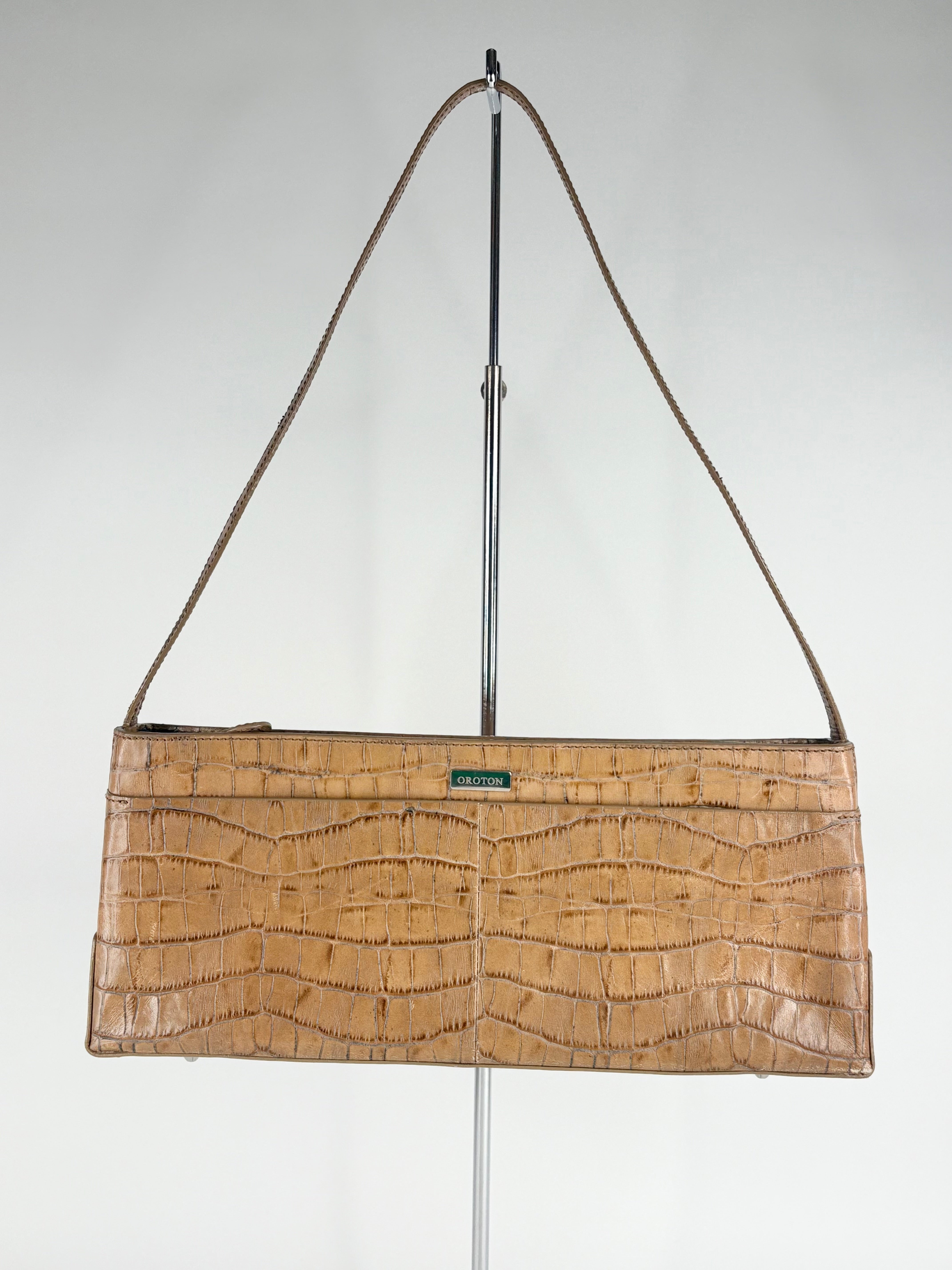 Brown crocodile-patterned handbag on a stand against a white background
