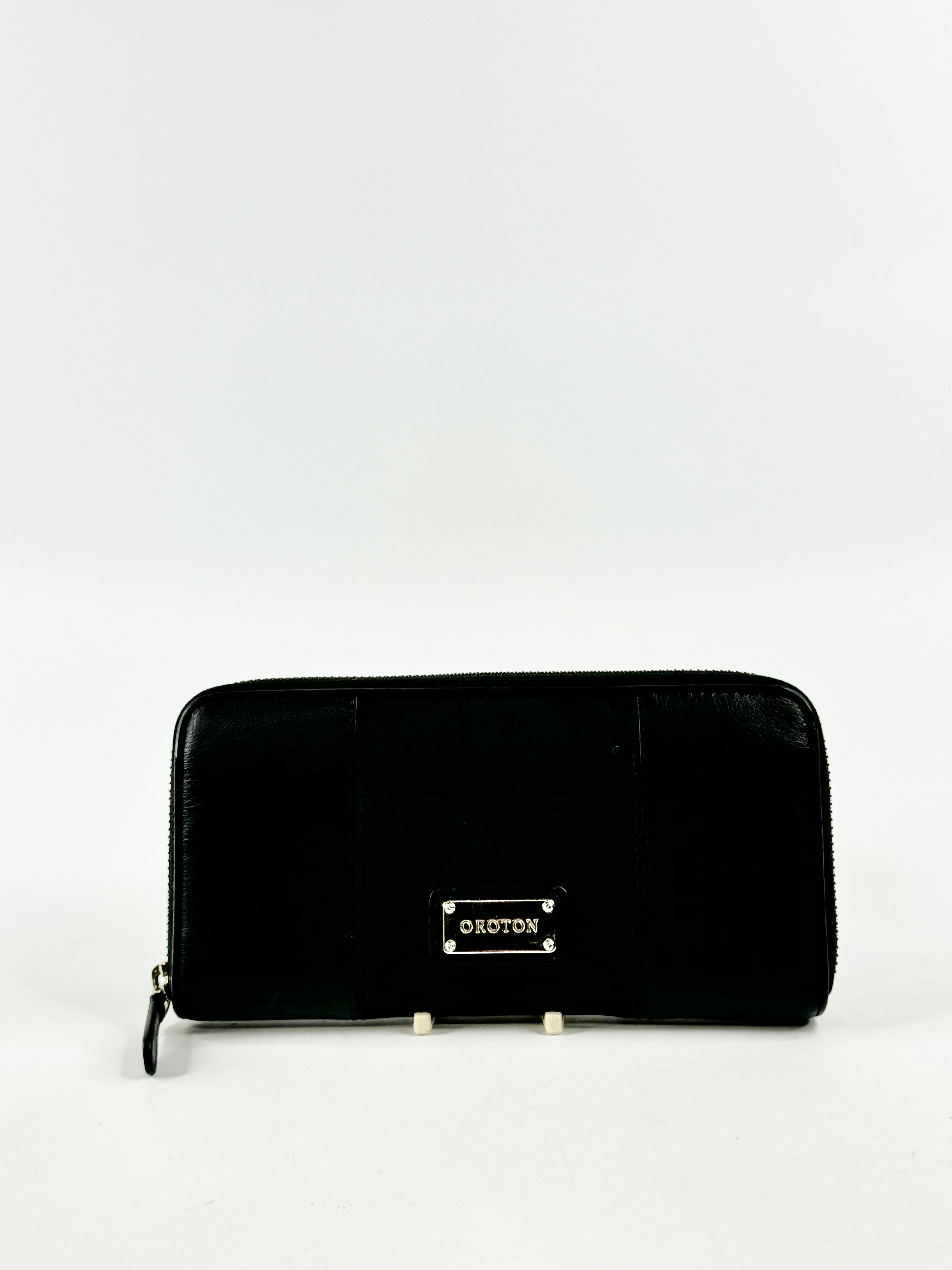 A black Oroton wallet with fabric and leather, featuring a zipper enclosure and brand monogram.