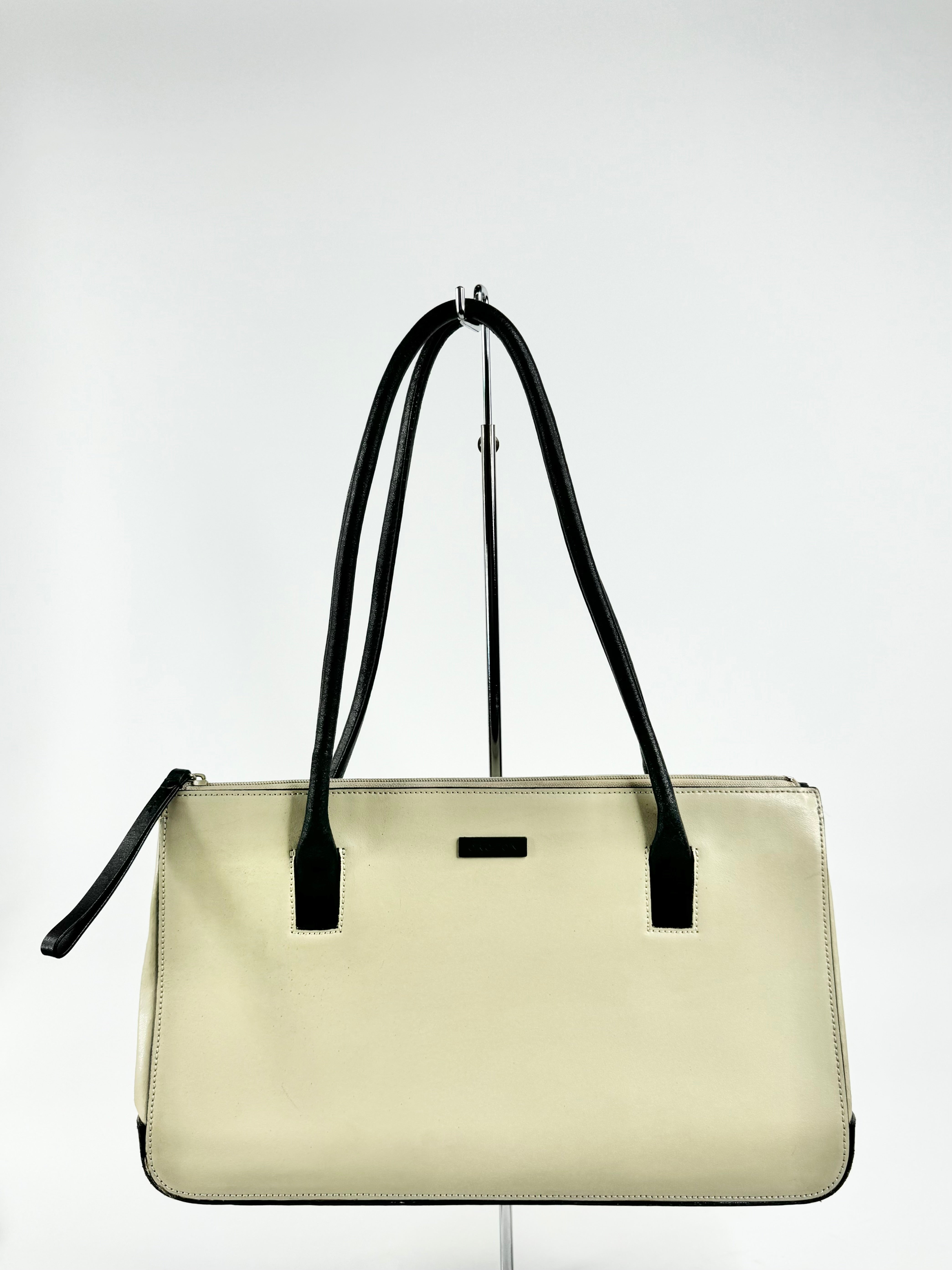 A structured rectangular shoulder bag with black handles and a zipper. The body is off green, and it has a black lining with a small zippered pocket.
