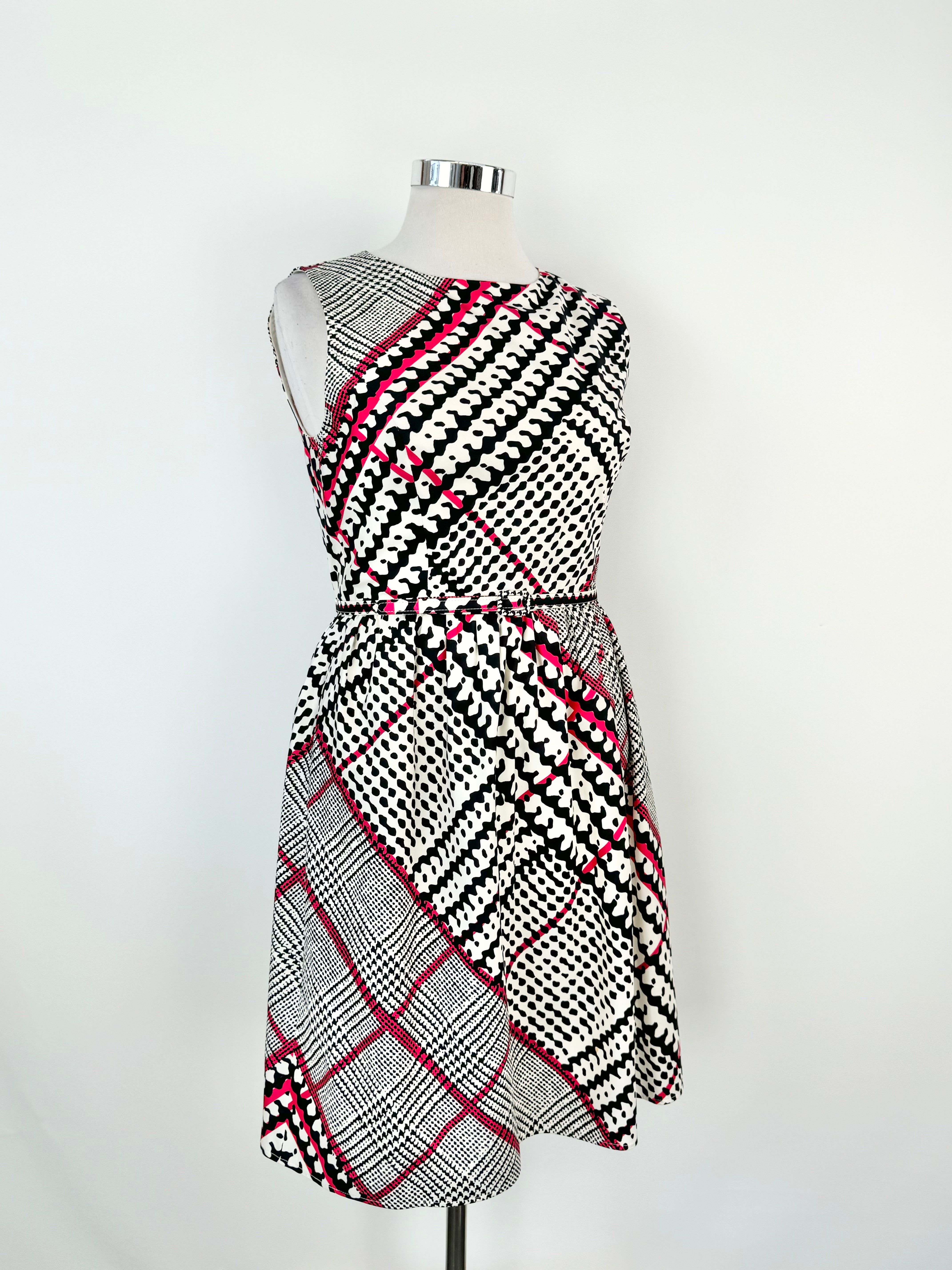 A silk midi dress with a geometric pattern in white, blue, and hot pink, featuring a rounded scoop neckline, zipper at the back, and a fine, small belted tie at the waist.
