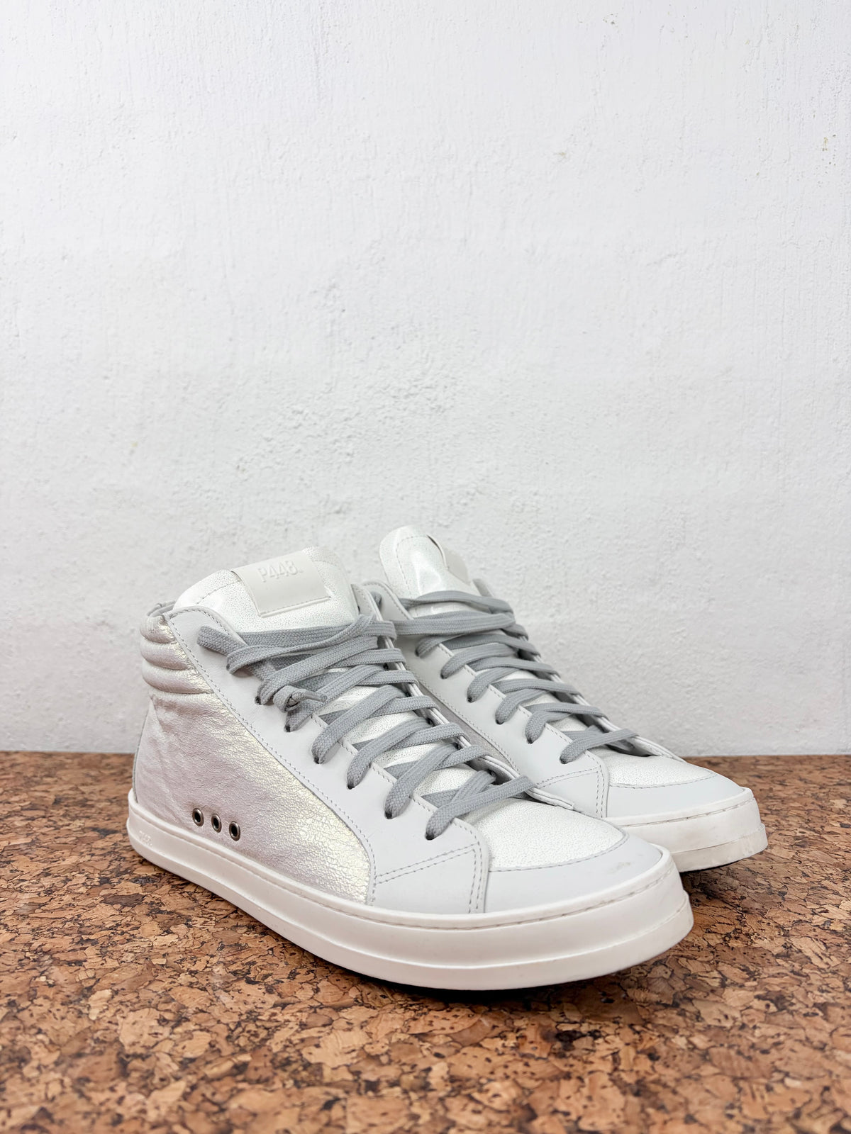 A pair of white high-top sneakers with light gray laces, displayed on a brown speckled countertop against a white textured wall.