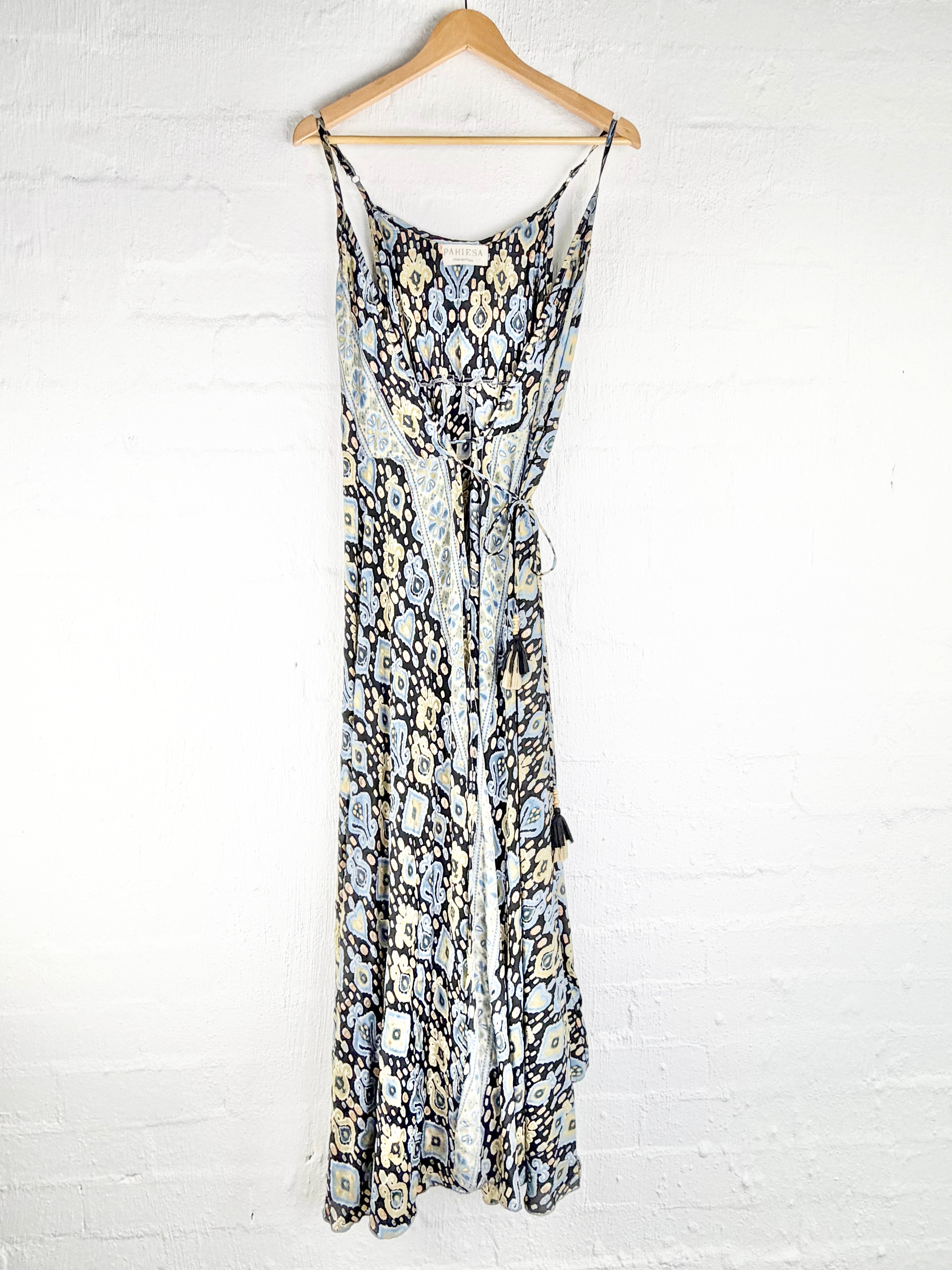A sleeveless maxi dress with a snakeskin print in black, beige, and gray, hanging on a wooden hanger against a white brick wall.