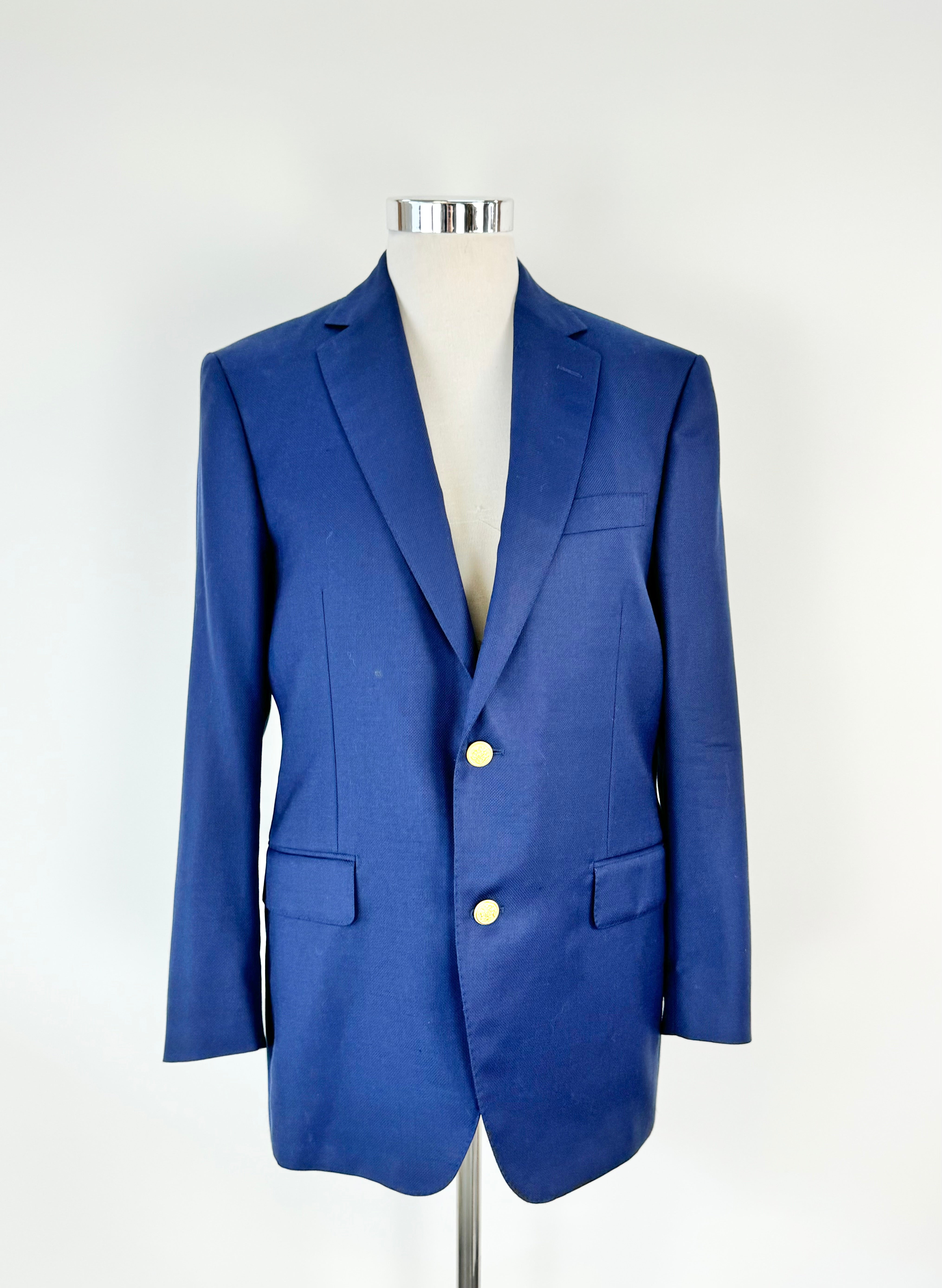 A deep cobalt blue blazer with gold toned buttons and a navy silky lining, displayed on a mannequin against a white background.