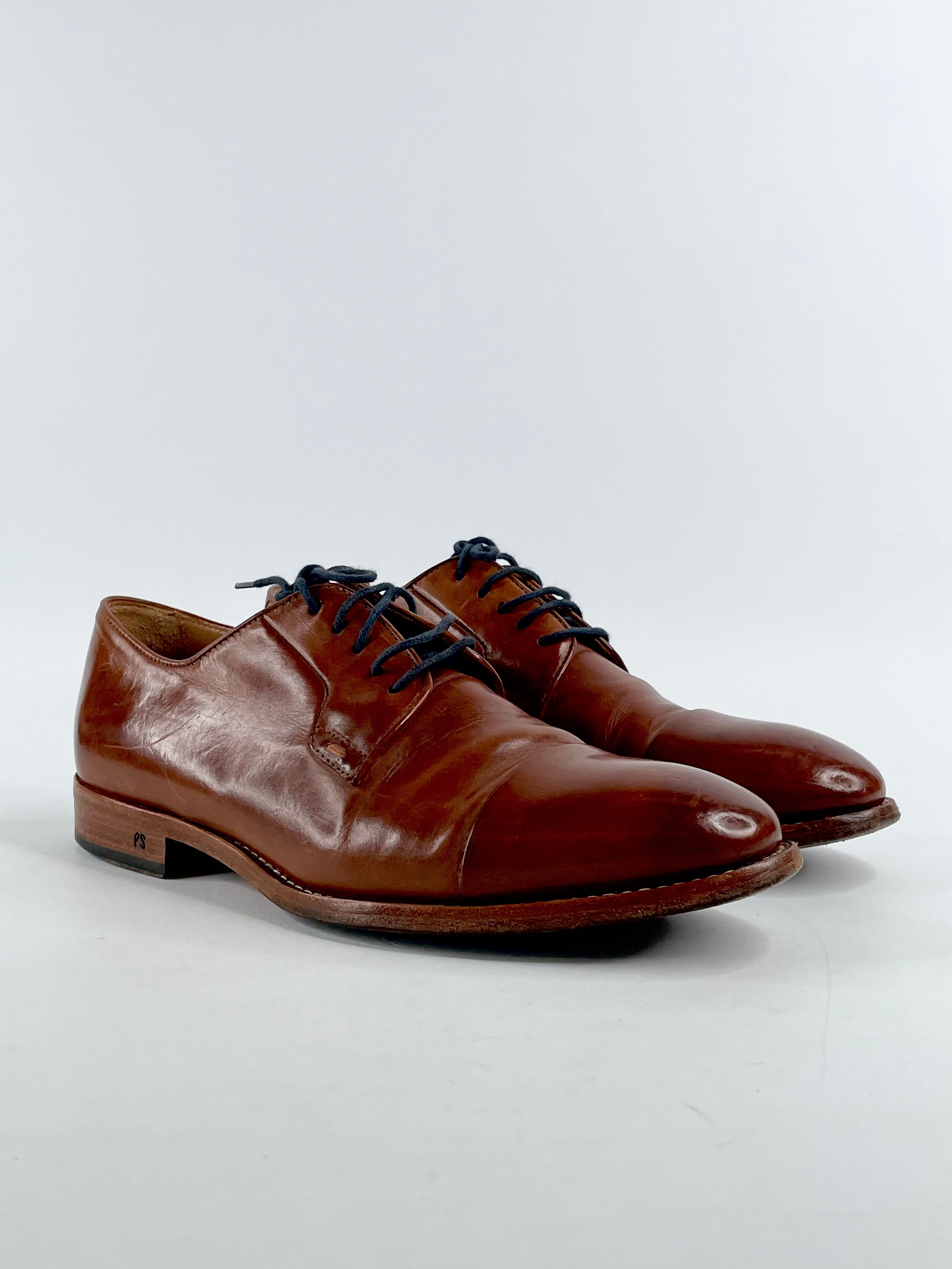 A pair of brown Paul Smith tan leather lace-up shoes with visible signs of wear on the soles.