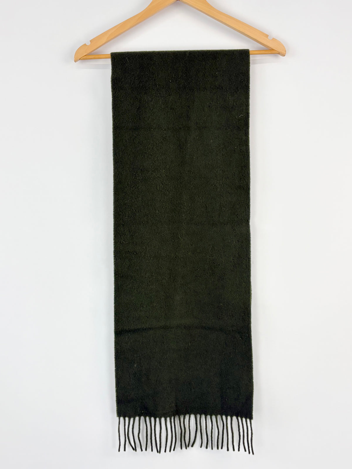 Green scarf with fringes on a wooden hanger against a white background