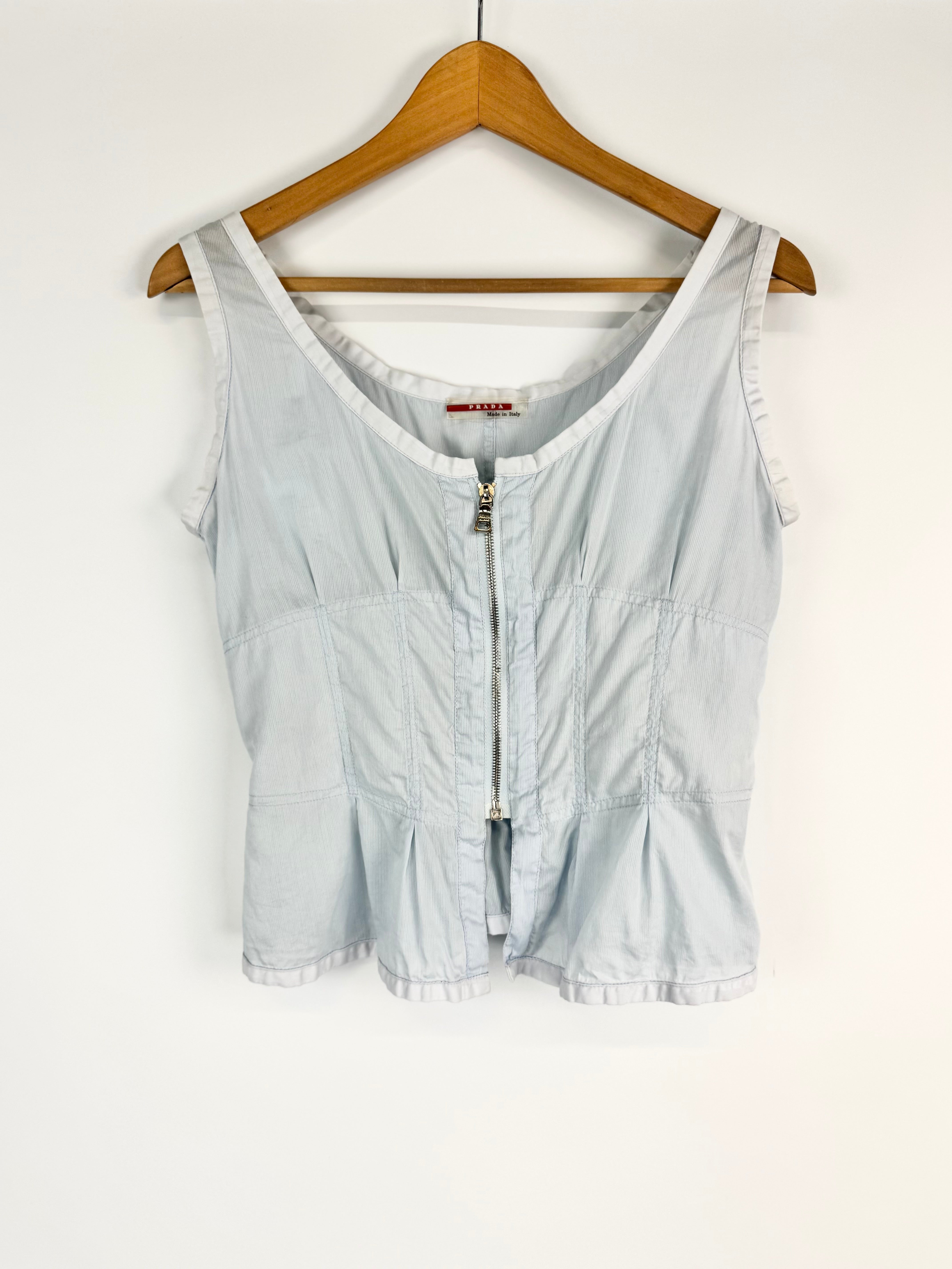 Light blue sleeveless top with zipper on a wooden hanger against a white background