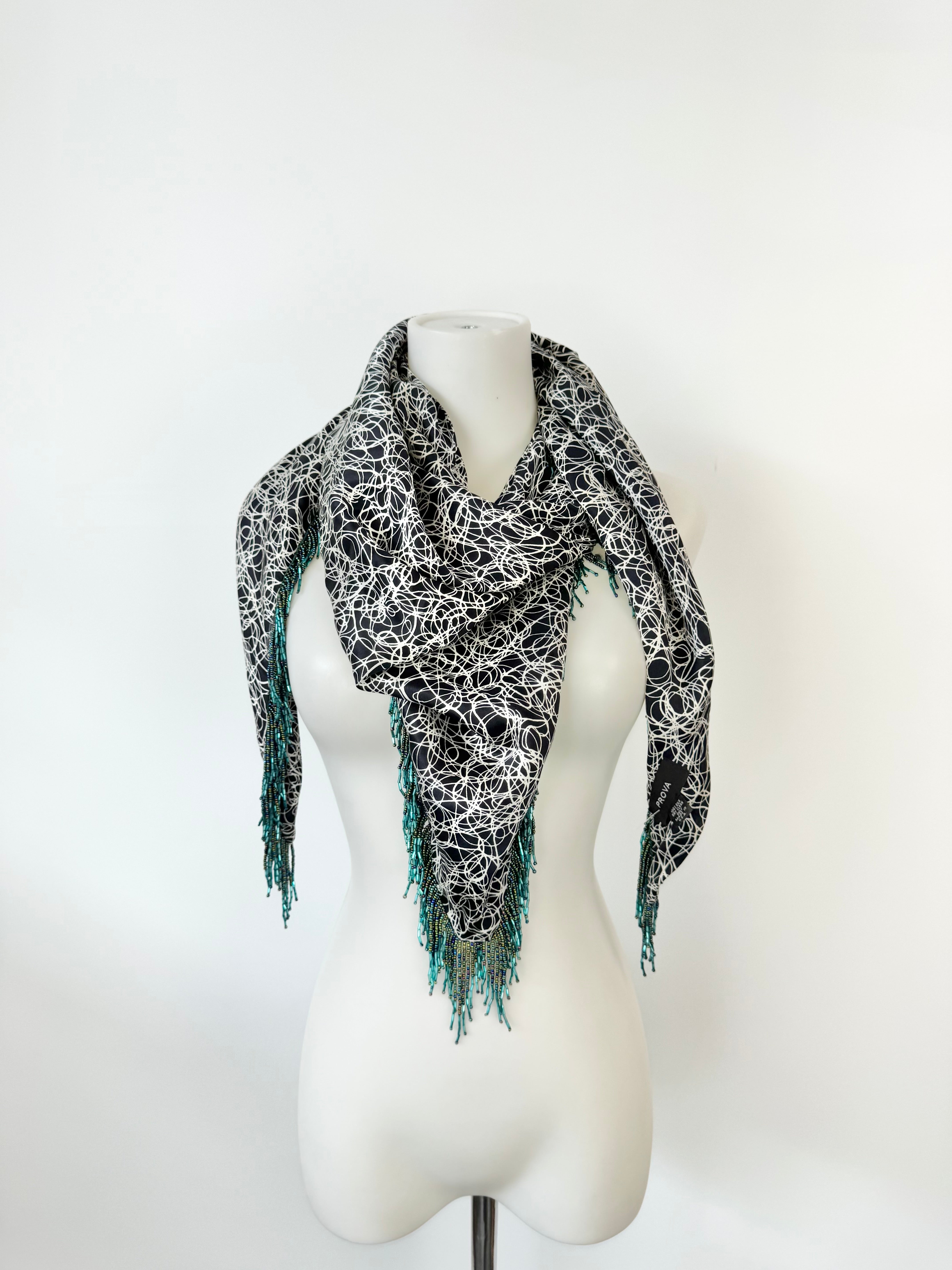 Black and white patterned scarf with teal edges on a mannequin against a white background
