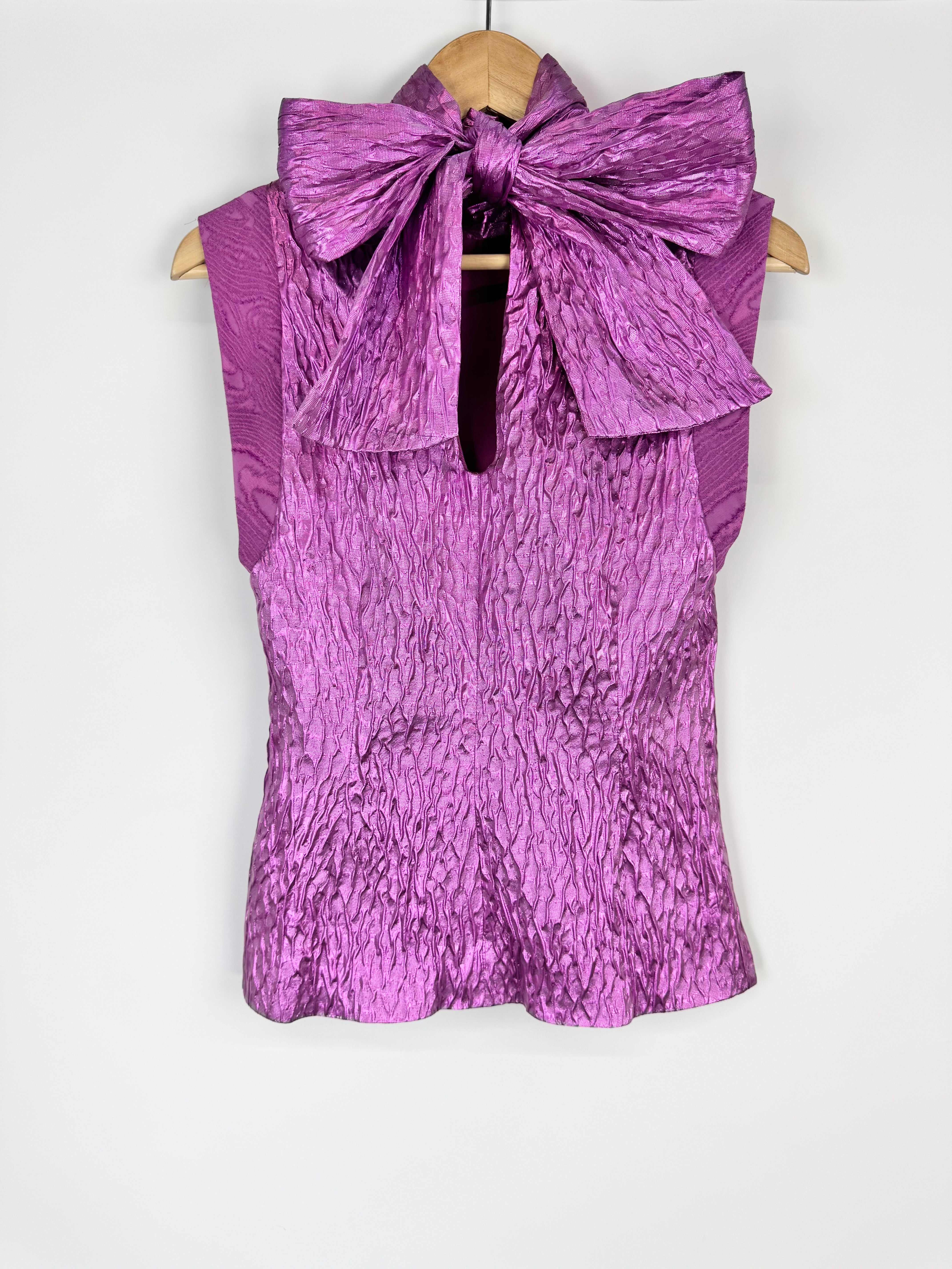 Purple textured blouse with a large bow on a hanger against a white background