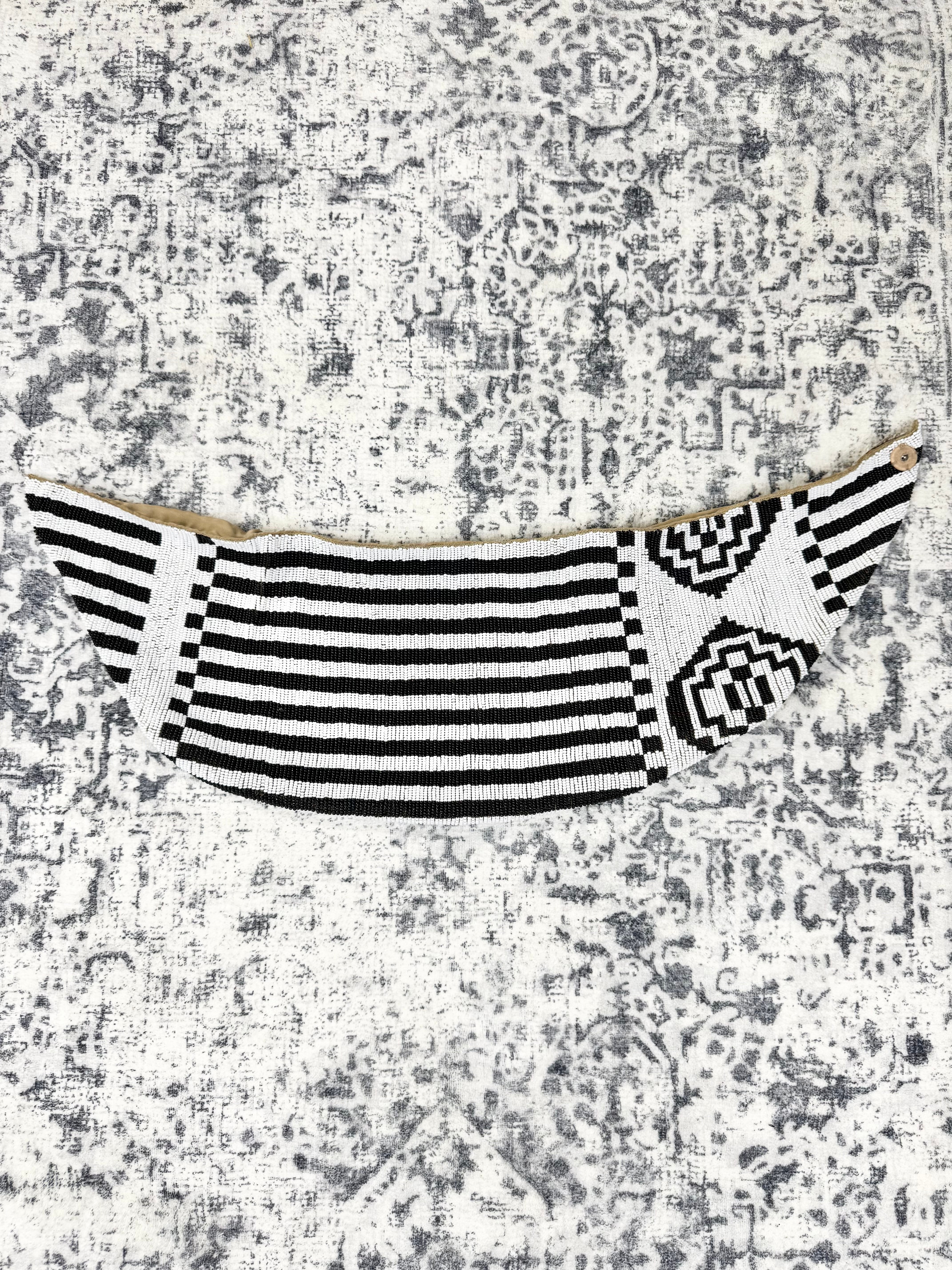 A black and white patterned fabric accessory, possibly a decorative belt or waist strap, laid flat on a distressed gray and white patterned background.