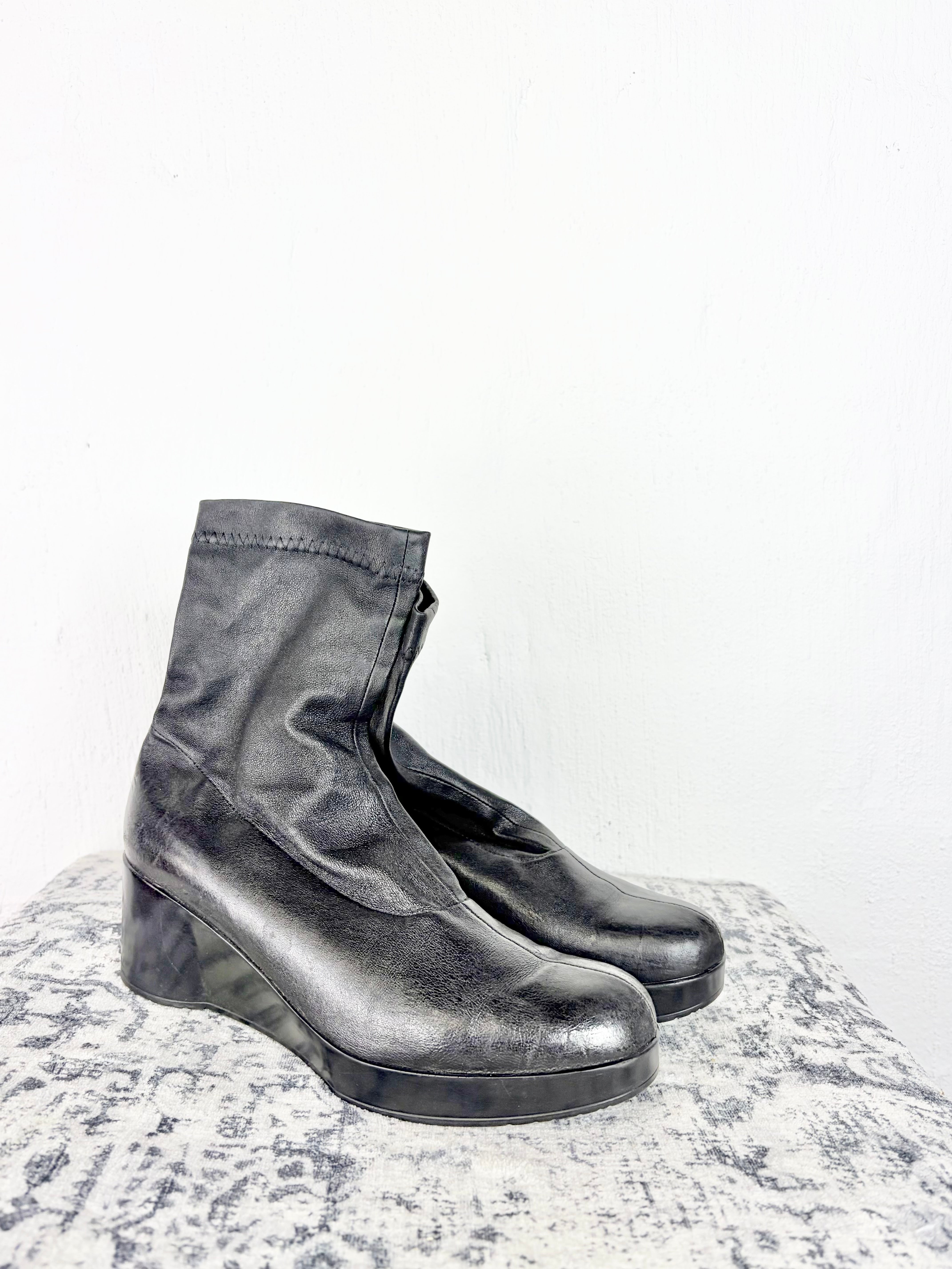 A pair of black leather ankle boots with chunky platform wedge heels, displayed on a textured gray surface against a plain white background.