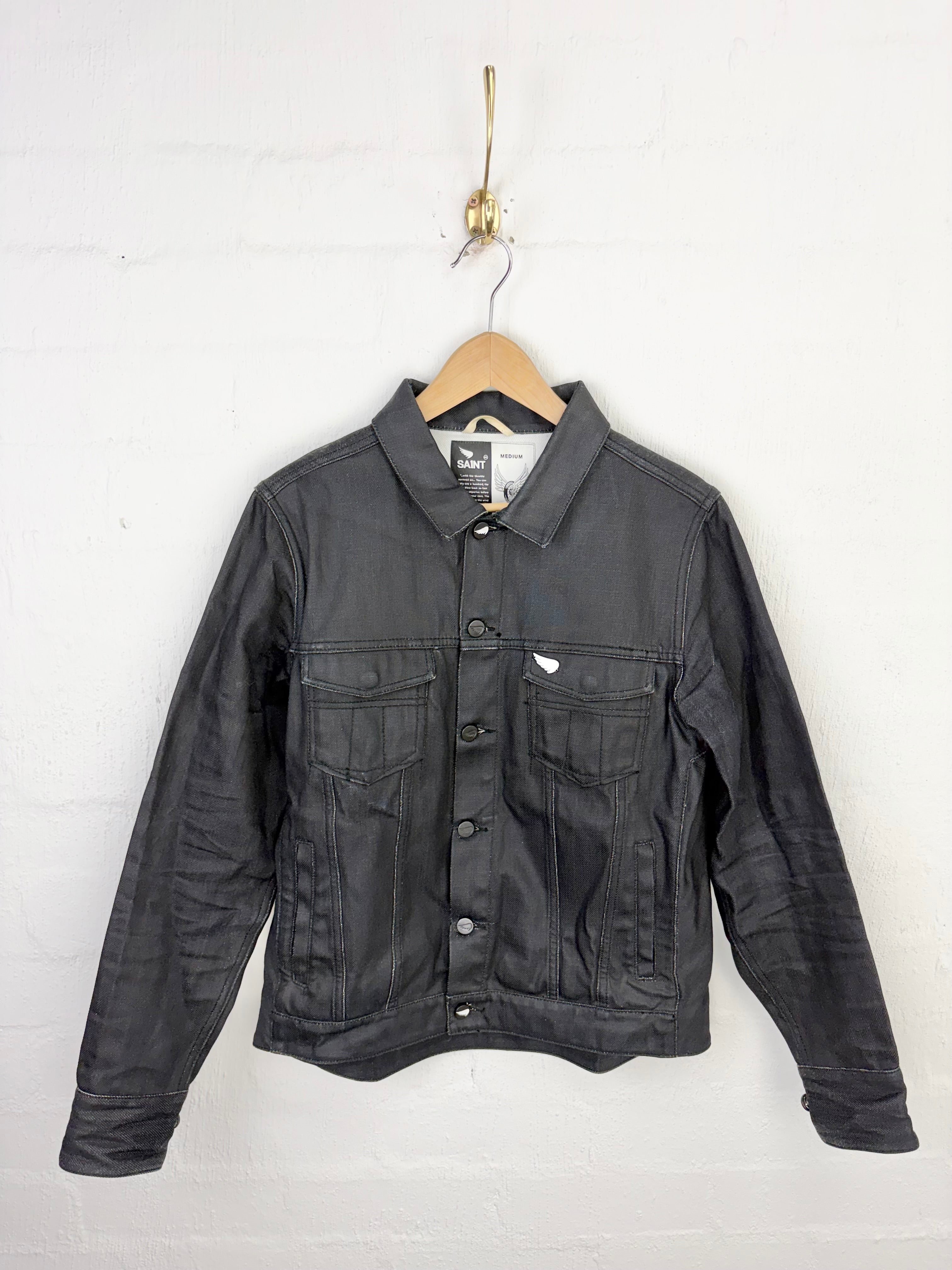A dark gray denim jacket hanging on a wooden hanger against a white painted brick wall.