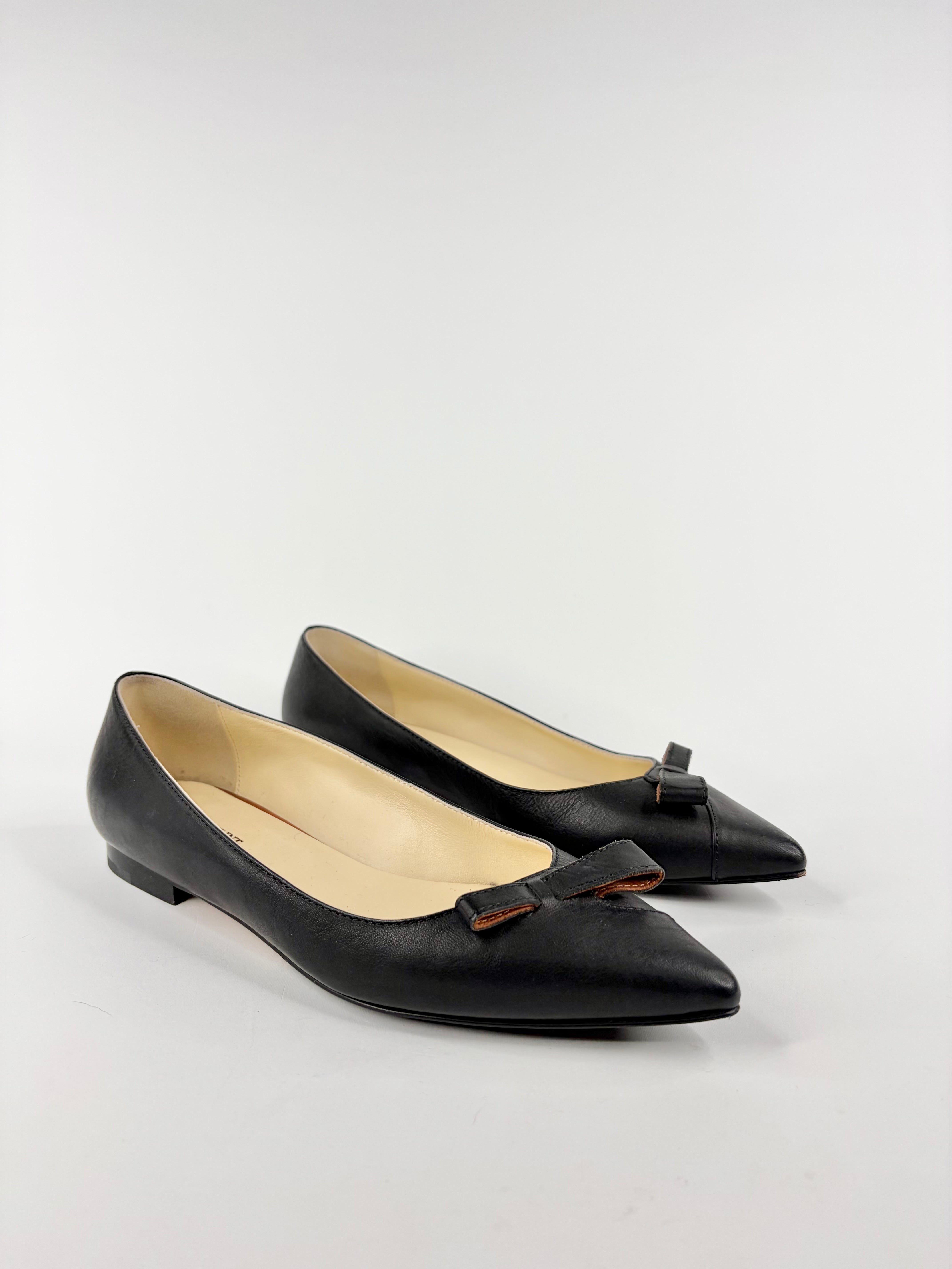 Pair of black pointed-toe flats with bow detail on a light gray background
