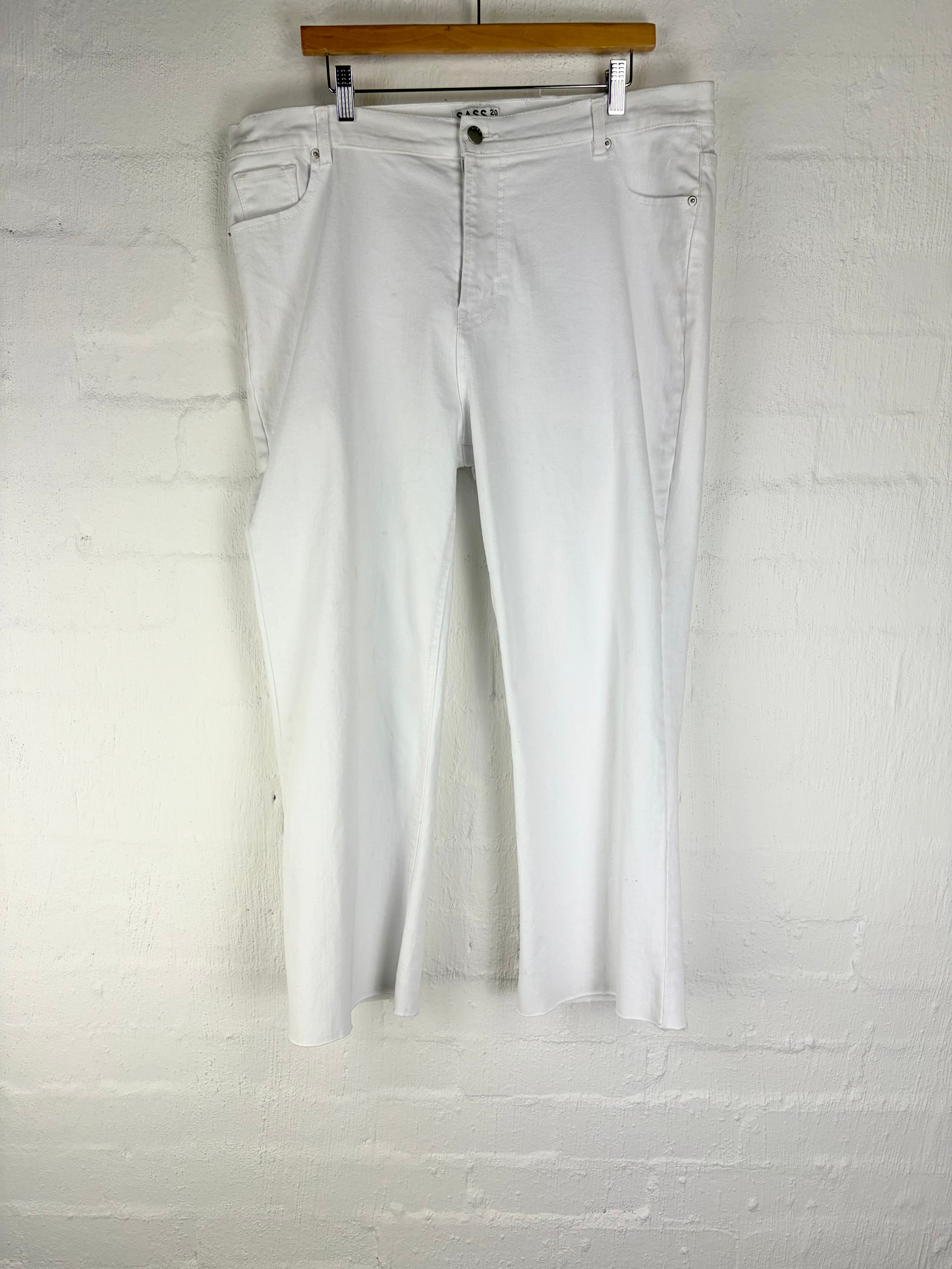 White cropped jeans hanging from a wooden hanger against a white painted brick wall.