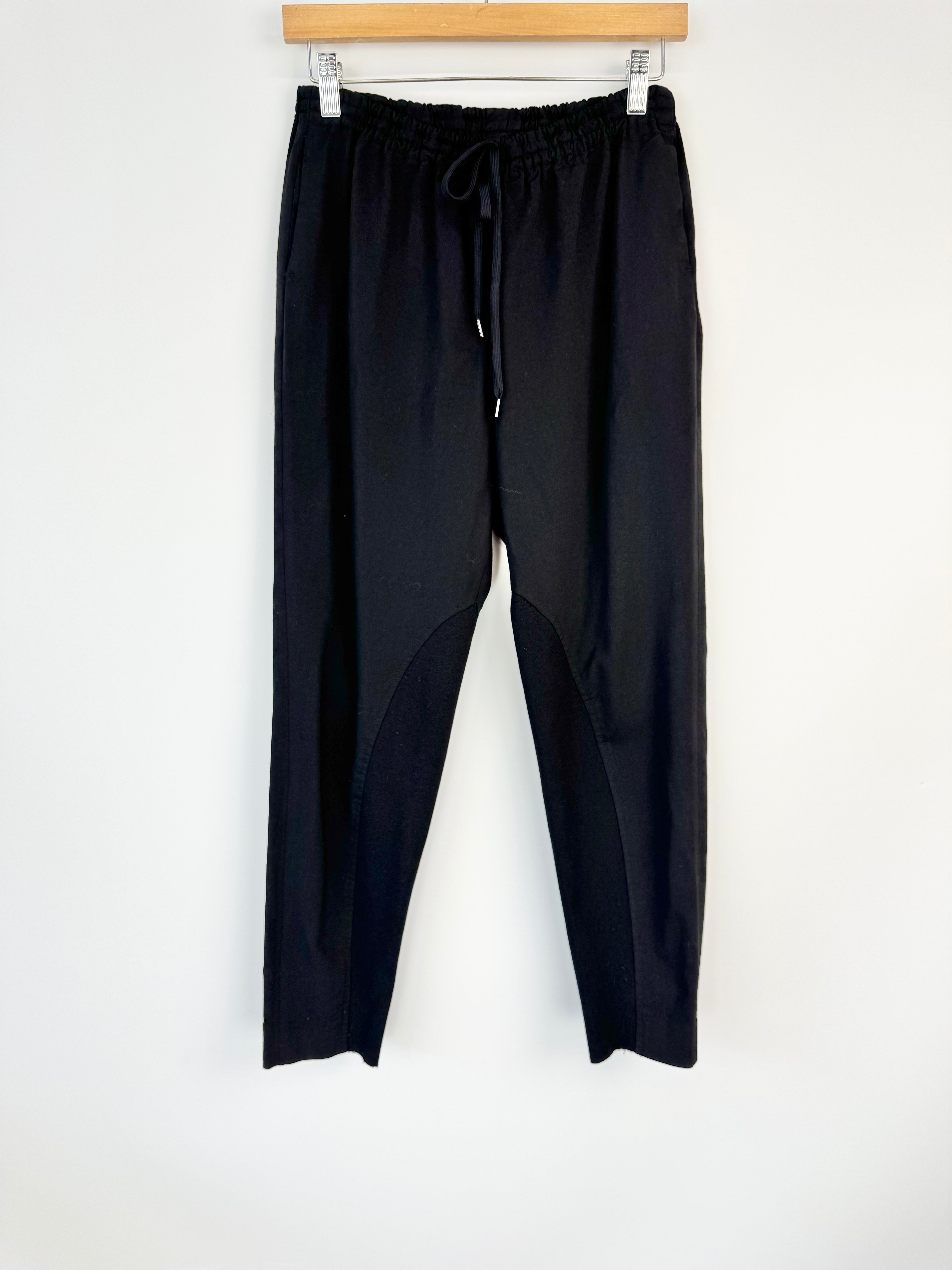 Black pants hanging on a wooden hanger against a white background