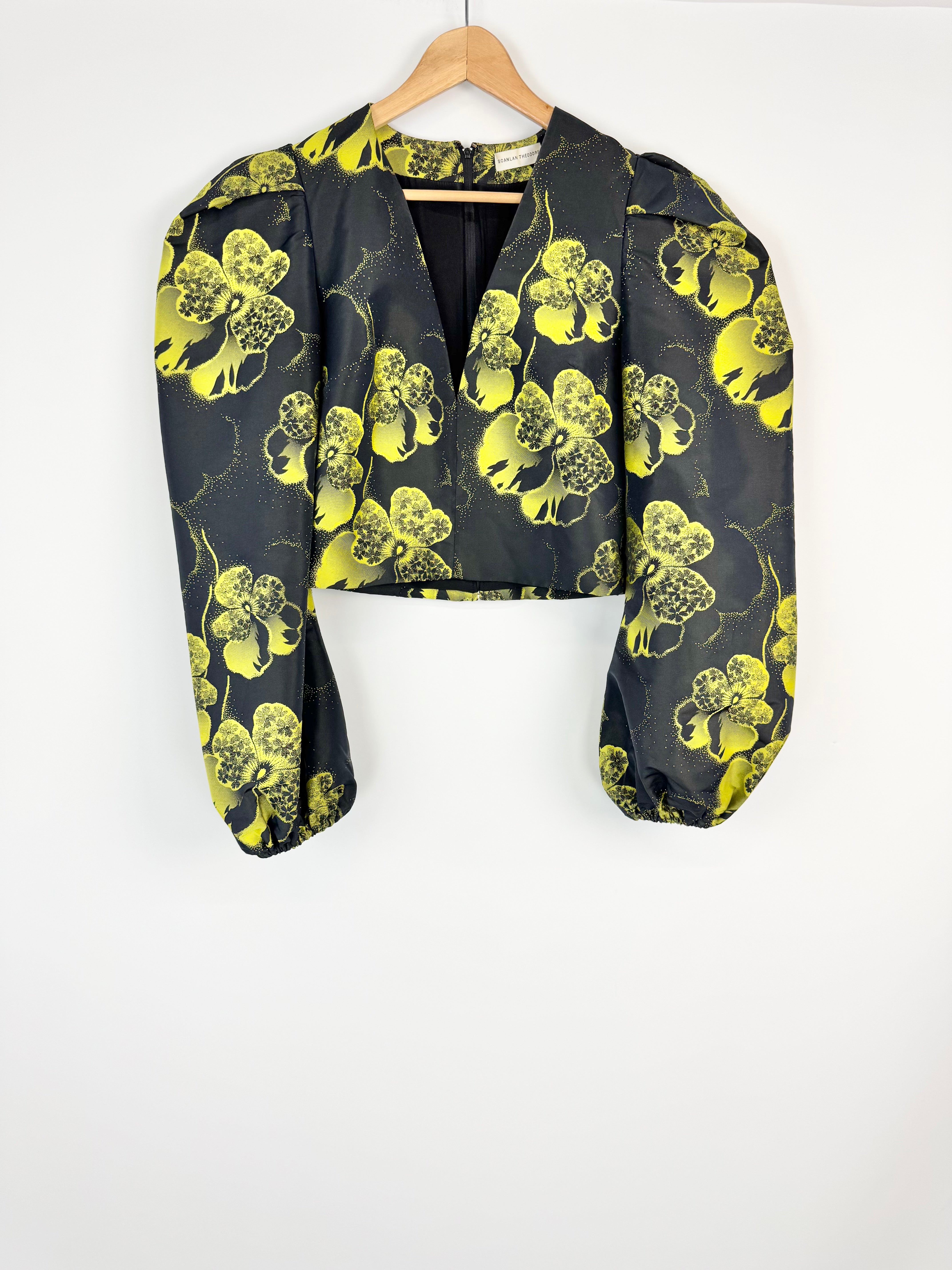 Black blouse with yellow floral pattern on a wooden hanger against a white background