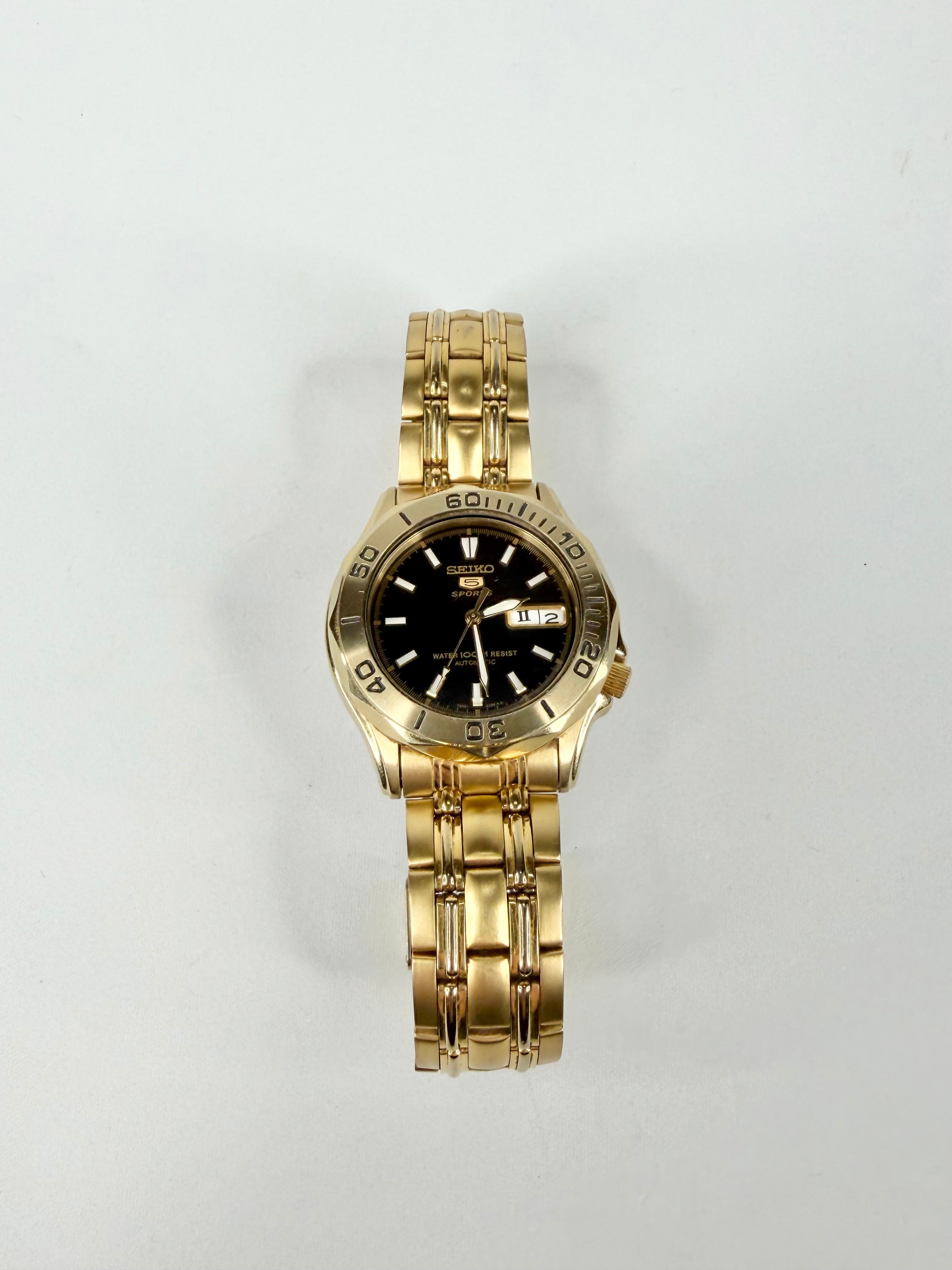 Gold wristwatch with a black face on a light gray background