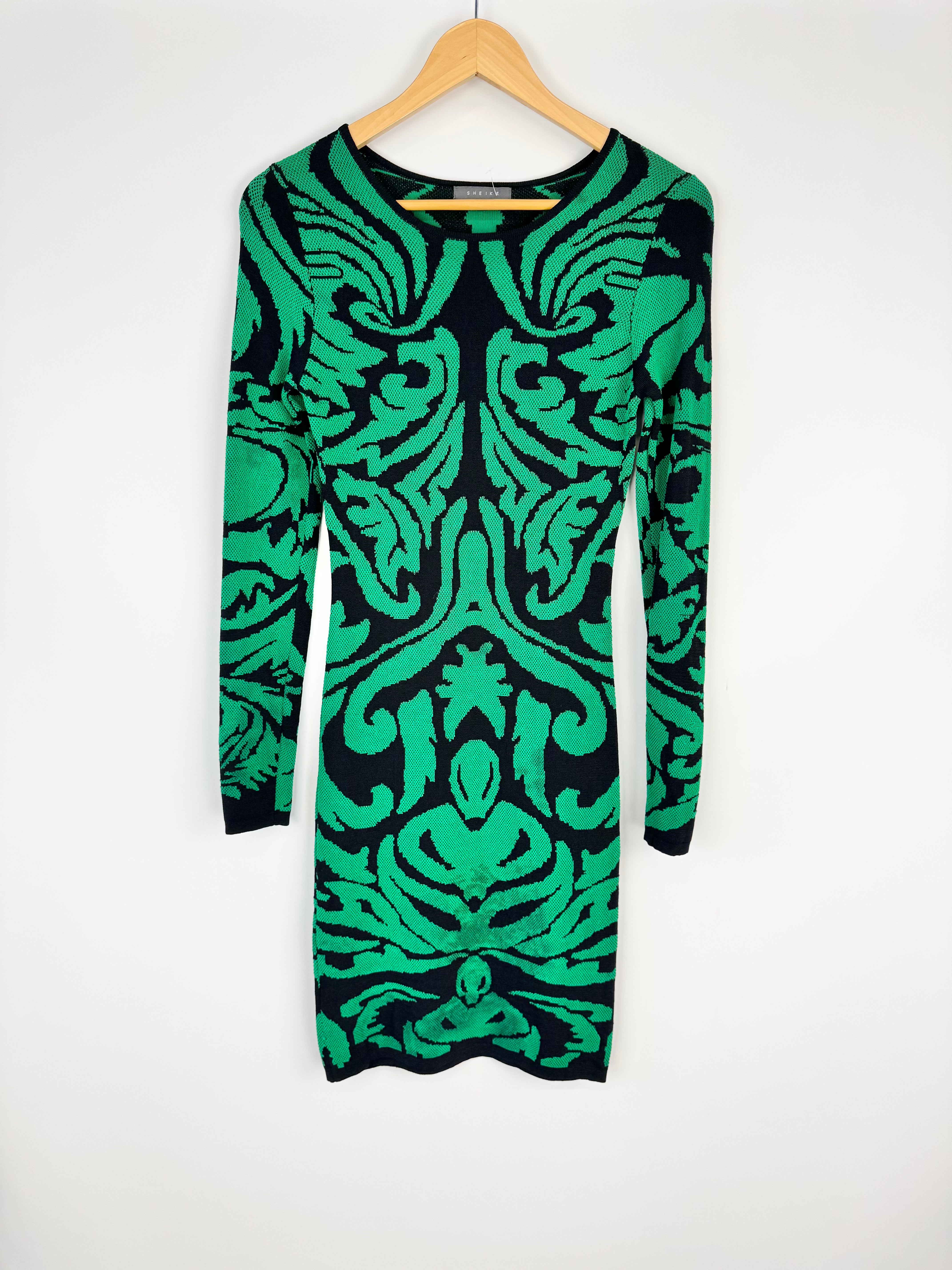 Green and black patterned dress on a wooden hanger against a white background
