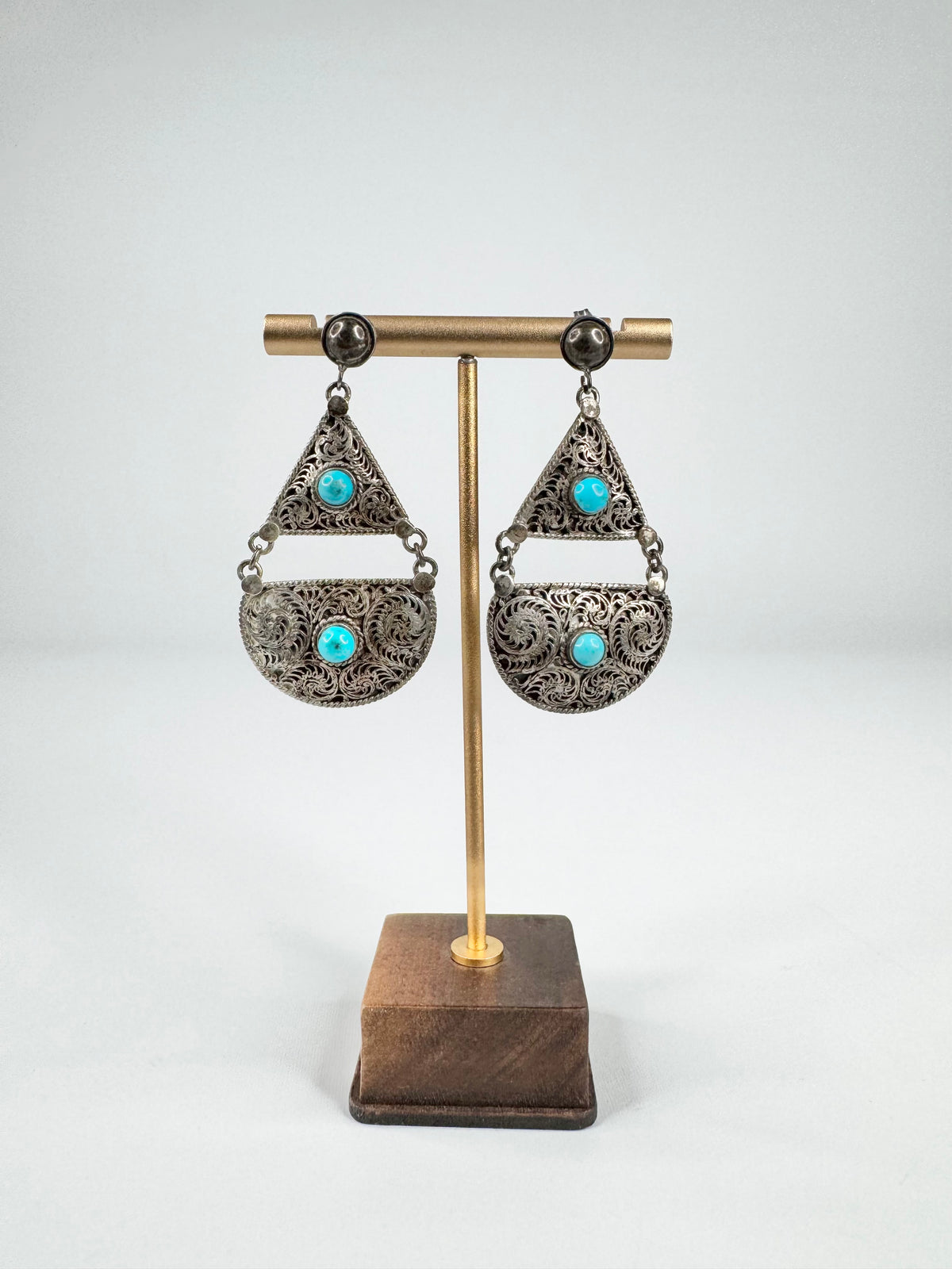 Pair of earrings with turquoise stones on a wooden stand against a white background