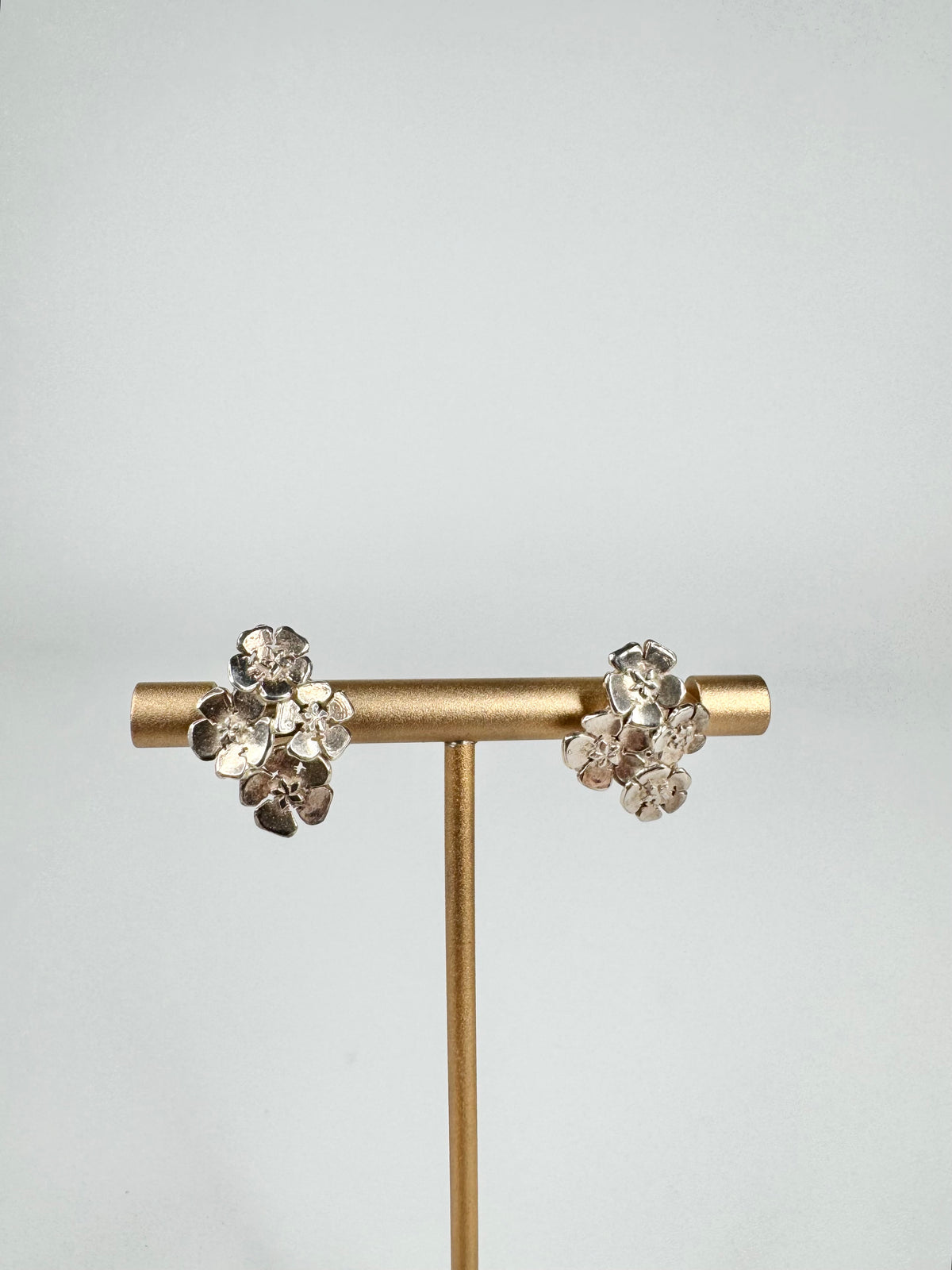 Pair of silver floral cluster earrings on a gold stand against a white background 