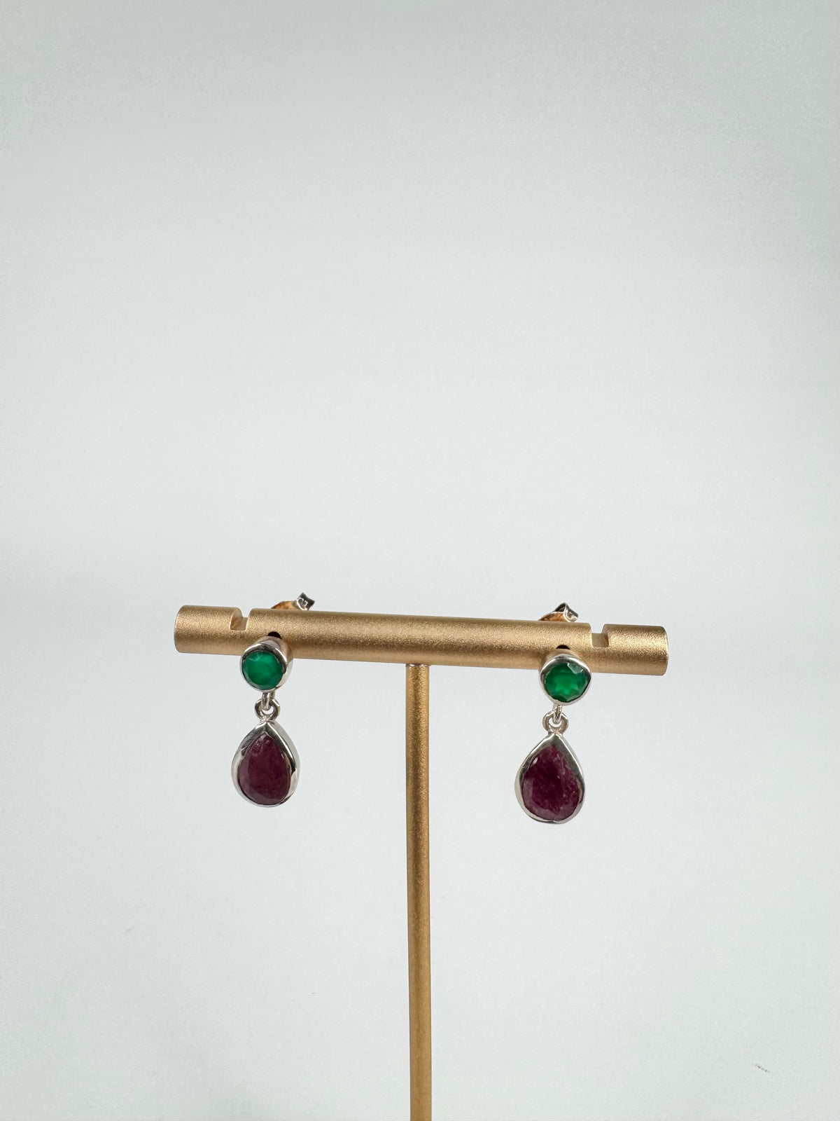 Pair of earrings with green and red stones on a gold stand against a white background