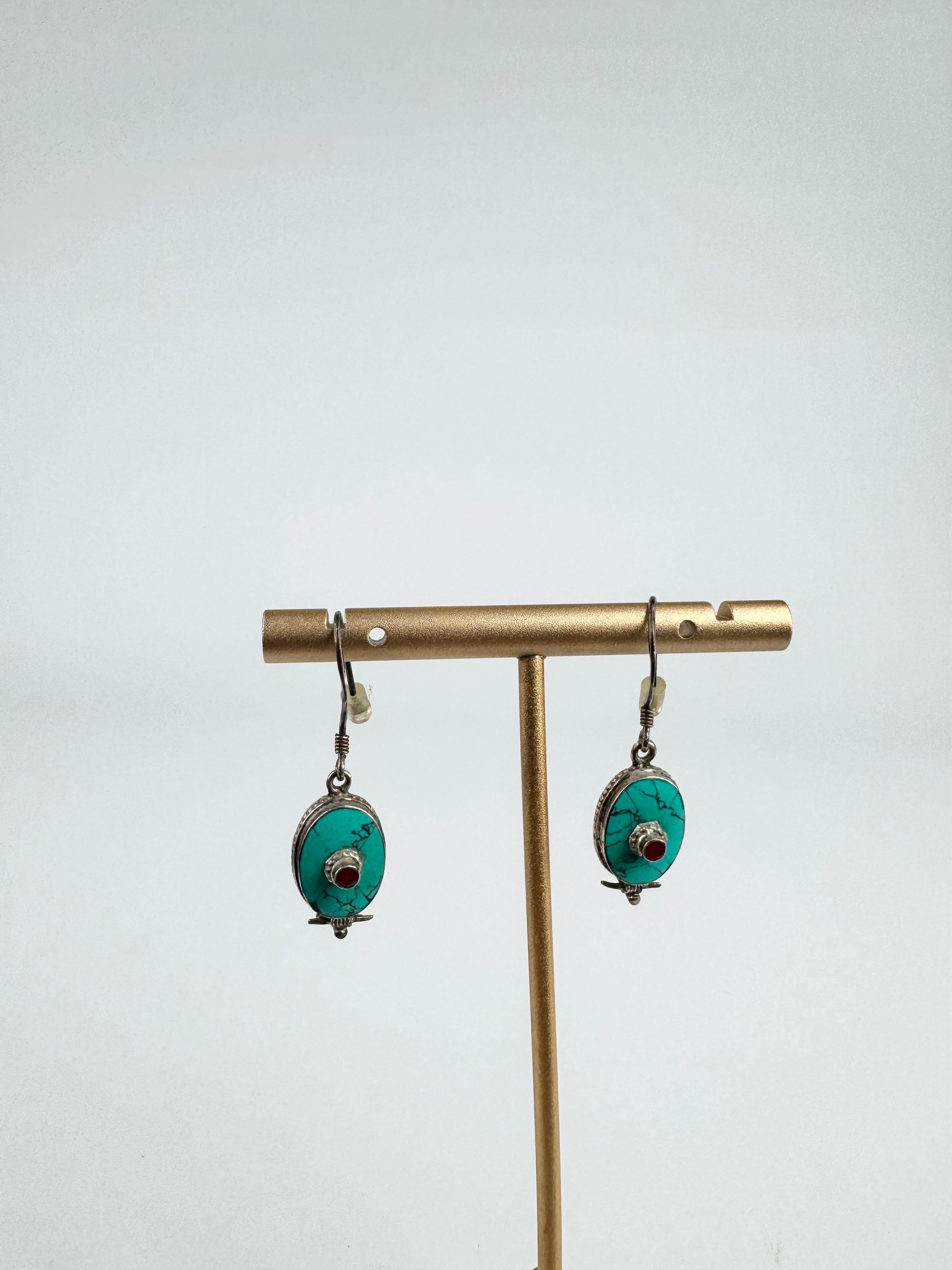 Pair of turquoise earrings on a gold earring stand against a white background