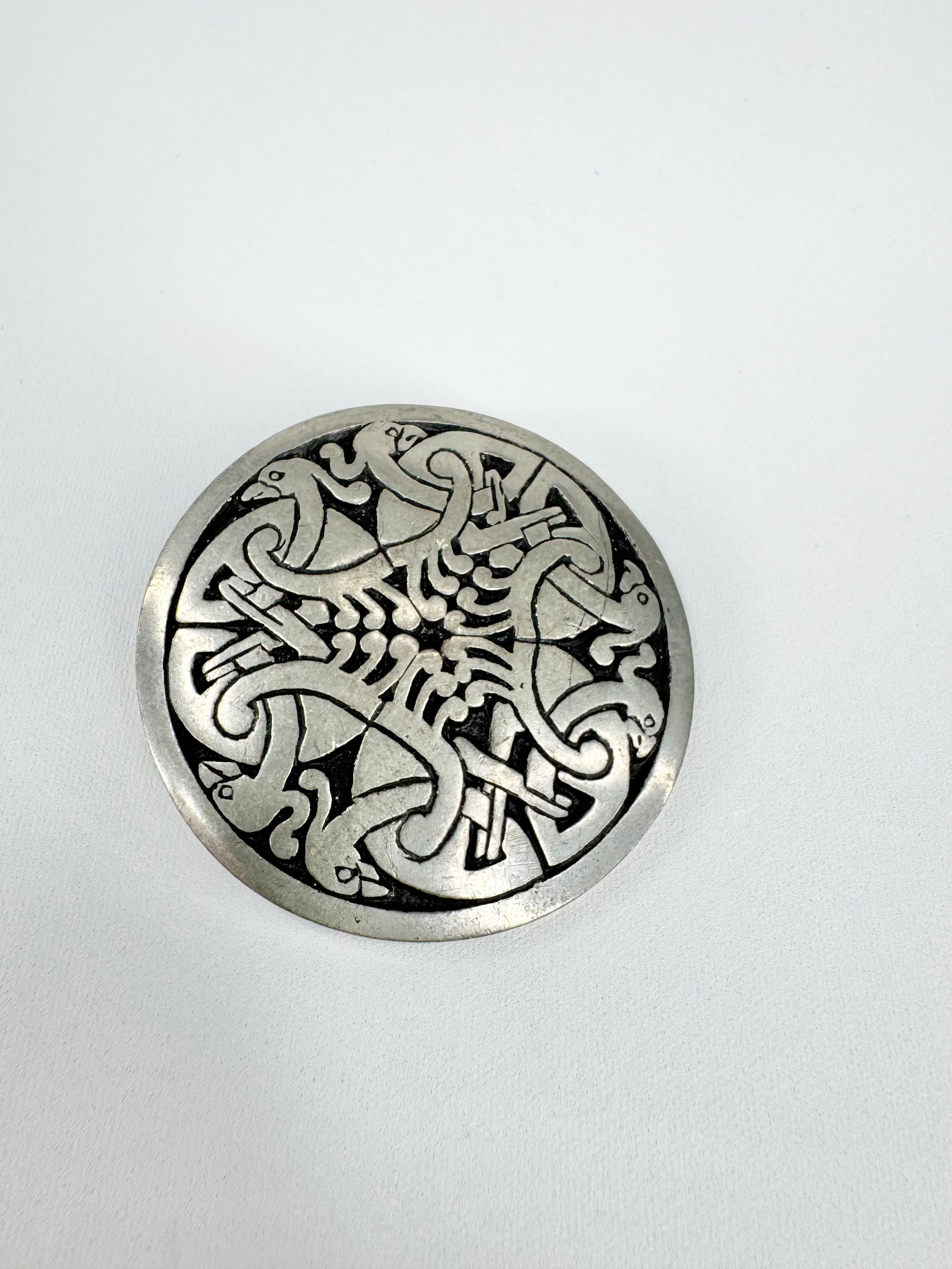 Silver circular pendant with intricate designs on a white background