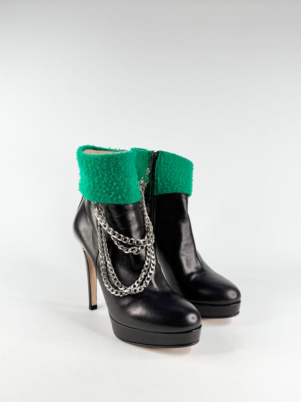 Black high-heeled boots with green cuffs and silver chains on a white background
