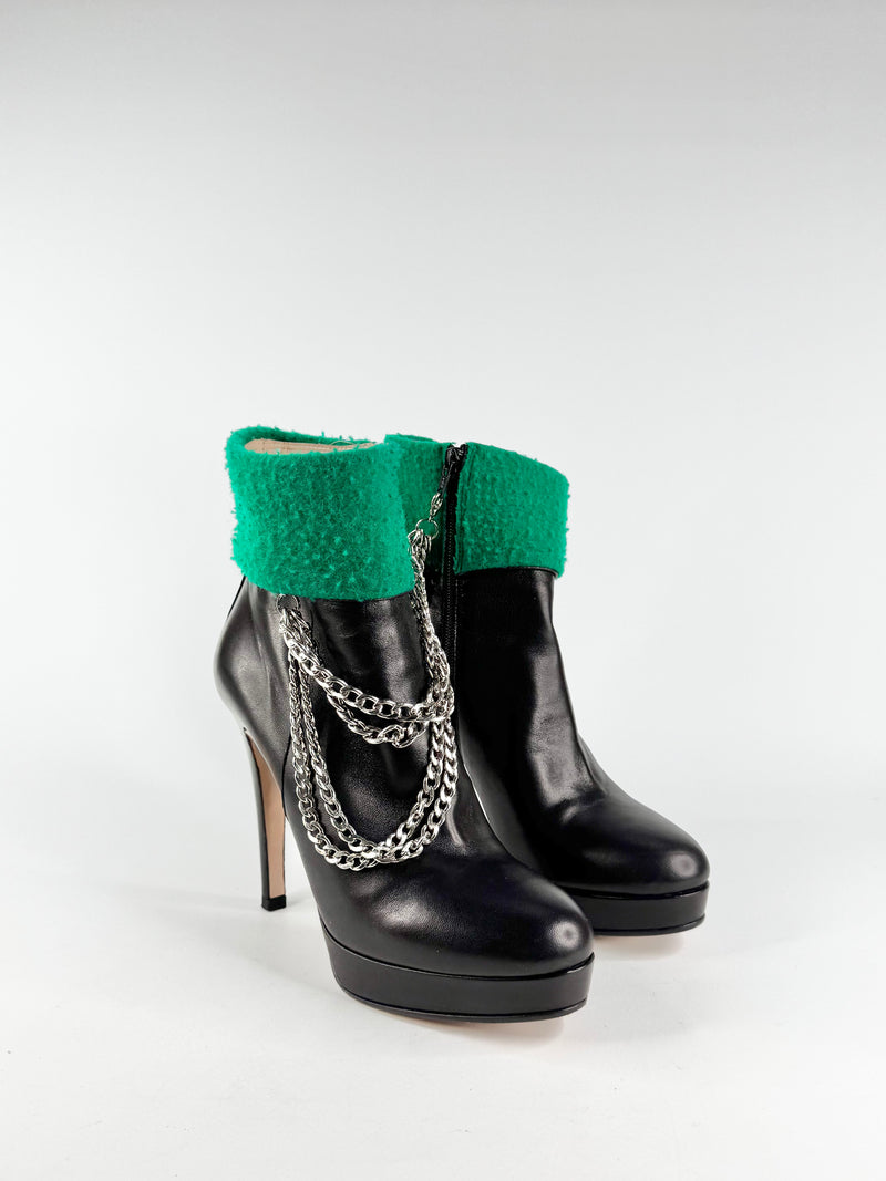 Black high-heeled boots with green cuffs and silver chains on a white background