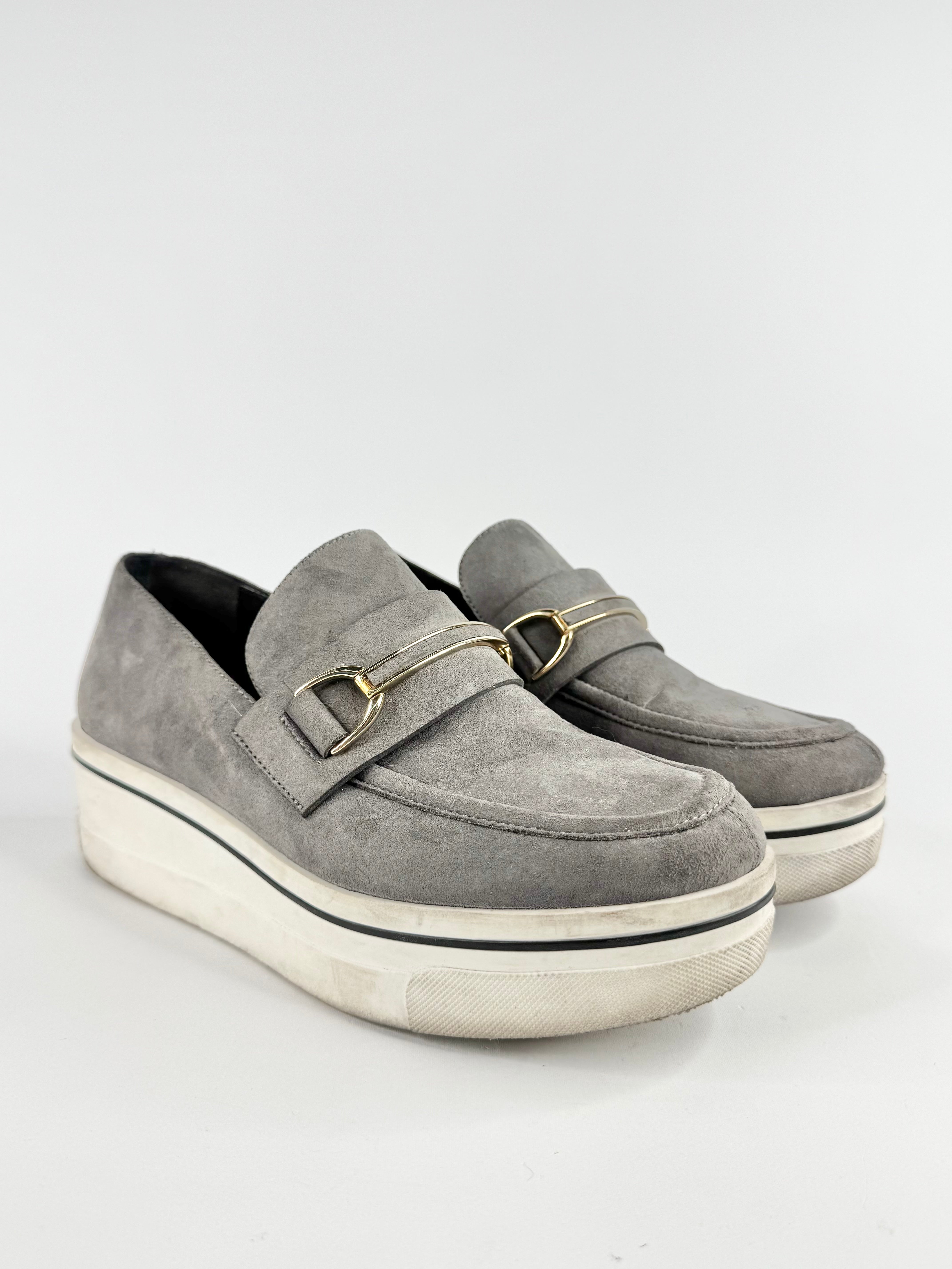 Gray suede loafers with gold buckles on a white background