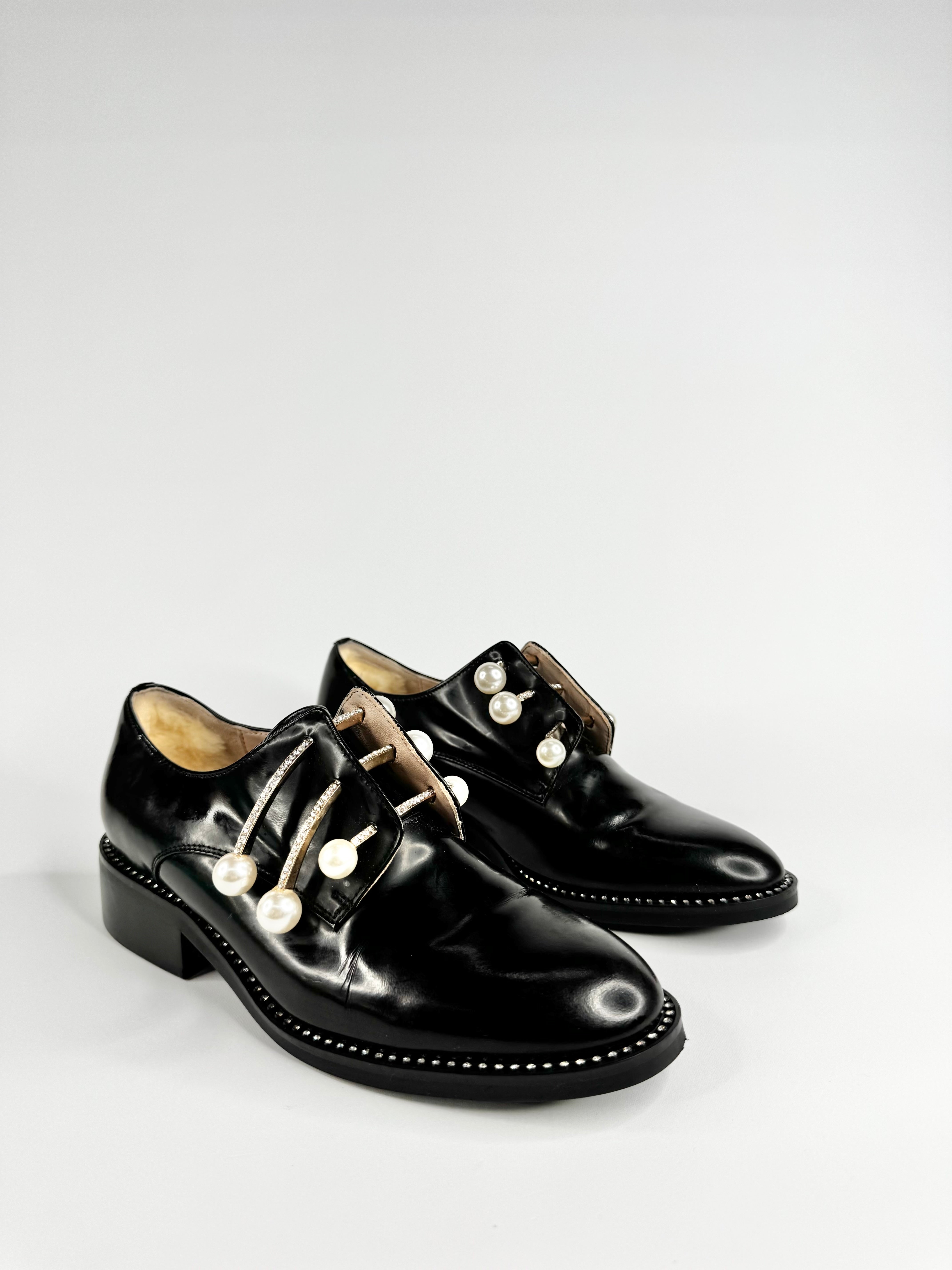 Pair of black leather shoes with white laces on a light gray background