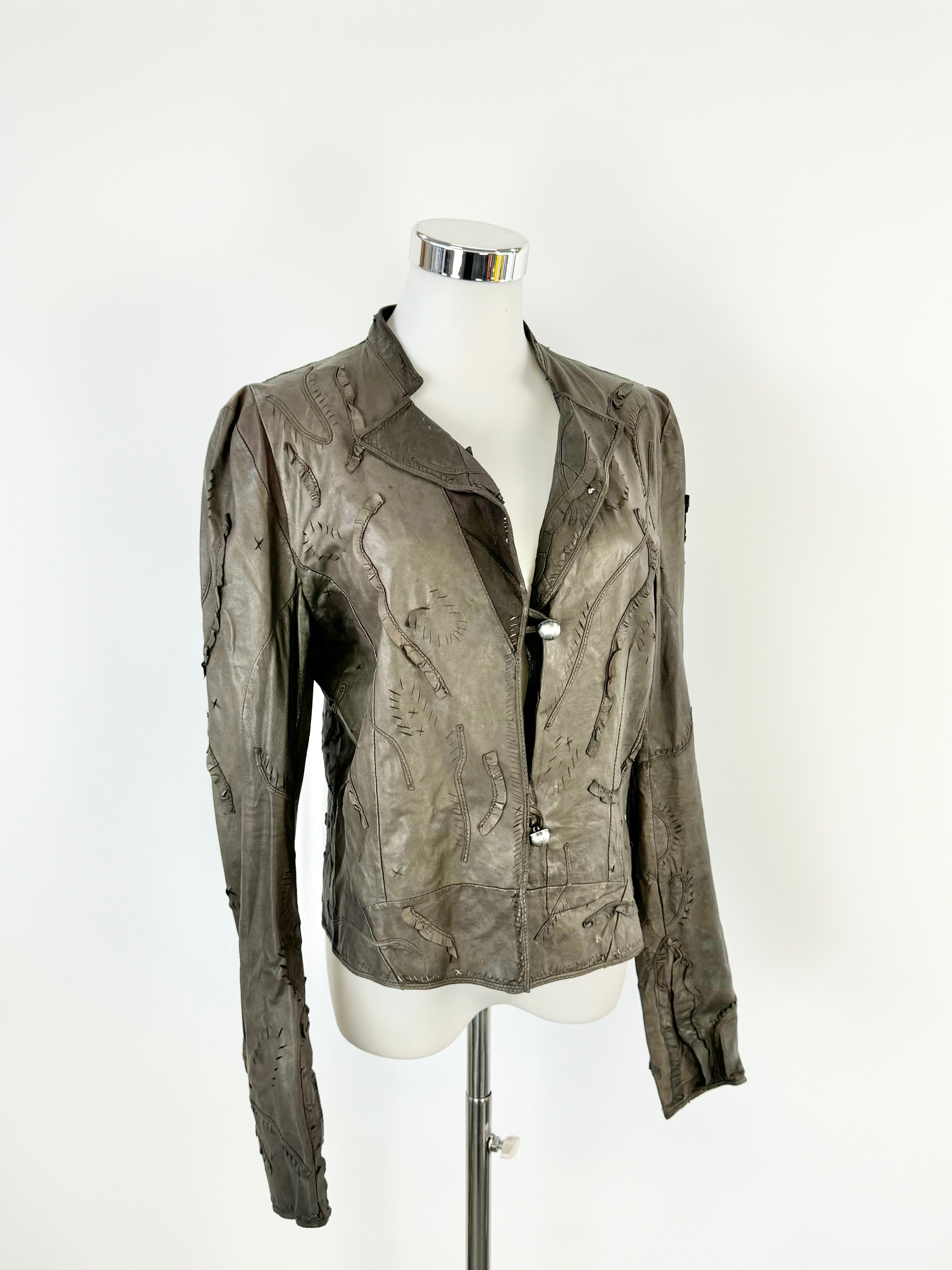 A brown leather jacket with lazer cut details and a mandarin collar on a mannequin.
