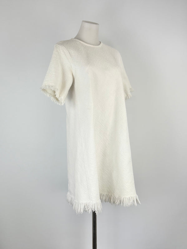 White dress with fringes on a mannequin against a gray background