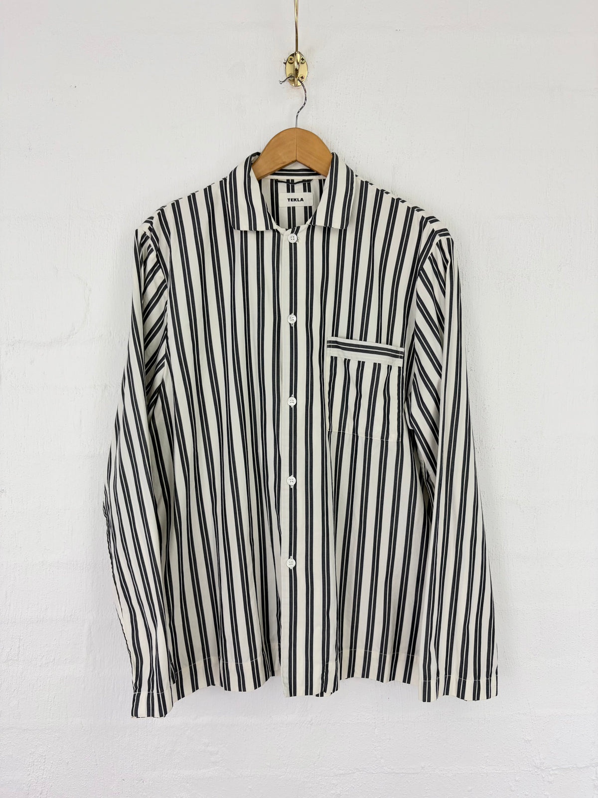 A long-sleeve button-up shirt with vertical black and off-white stripes, hanging on a wooden hanger against a white wall.