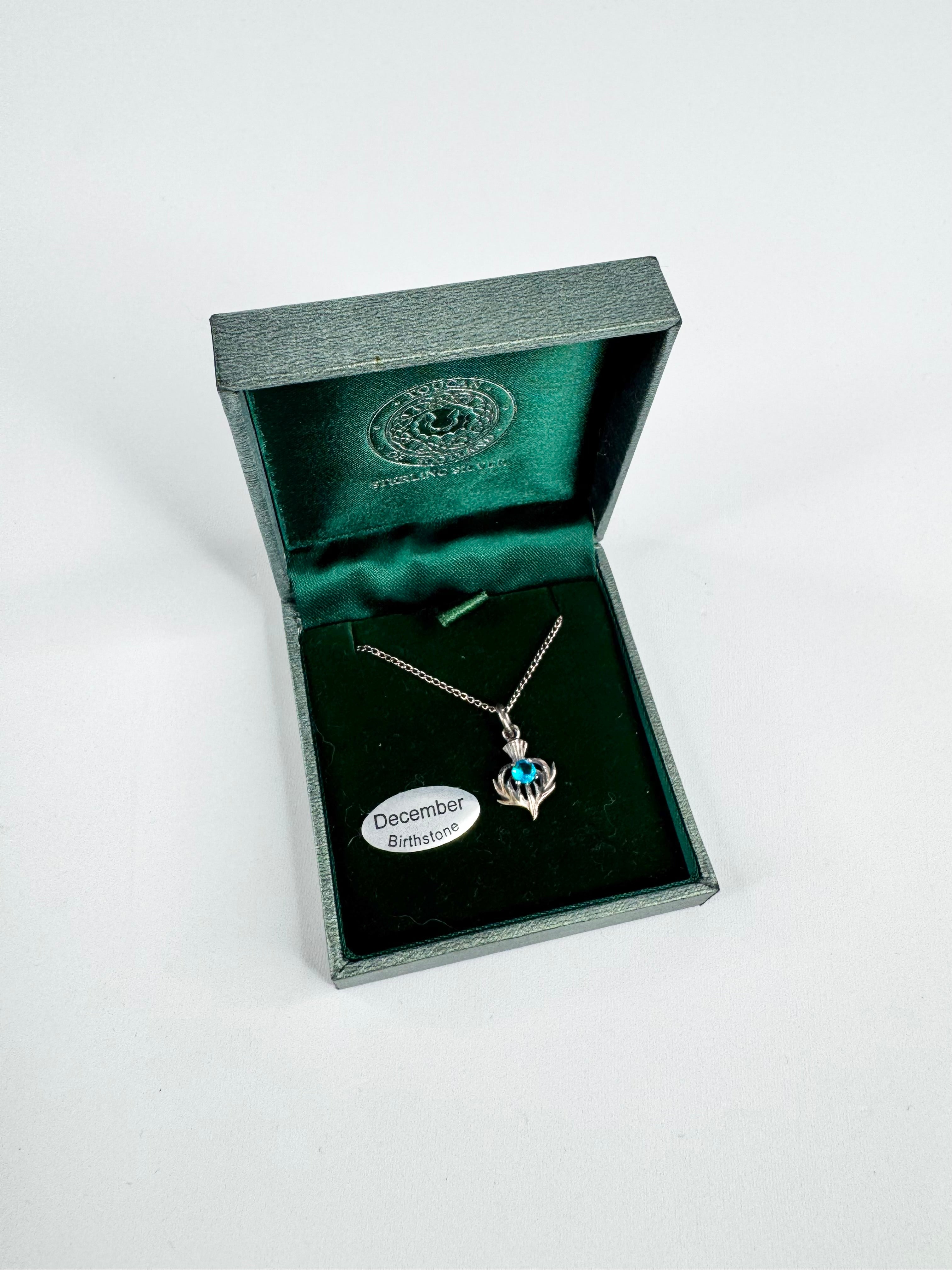 Jewelry box with a necklace featuring a blue gemstone and a December birthstone card.