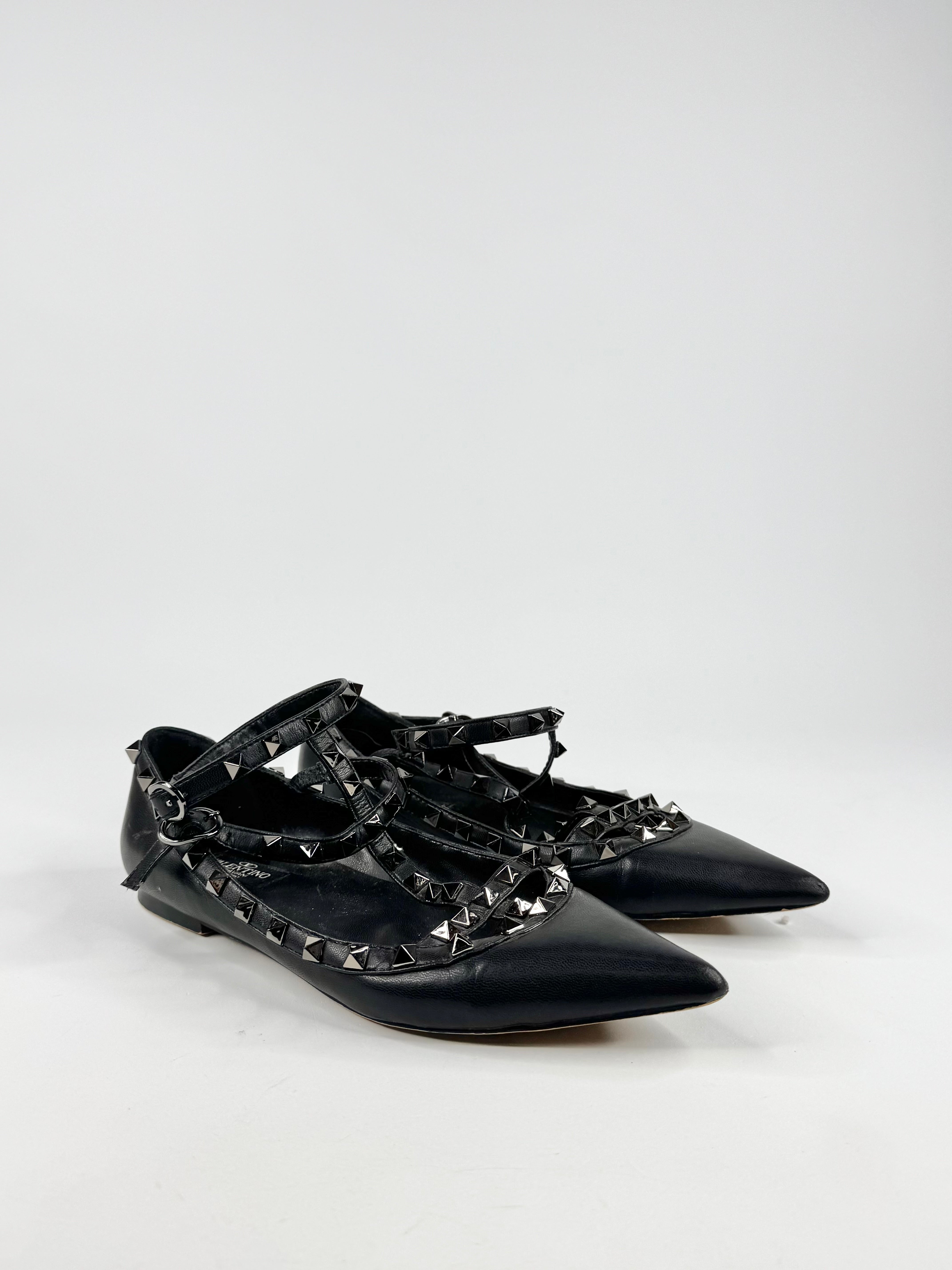 Black flat shoes with chain and stud details on a white background